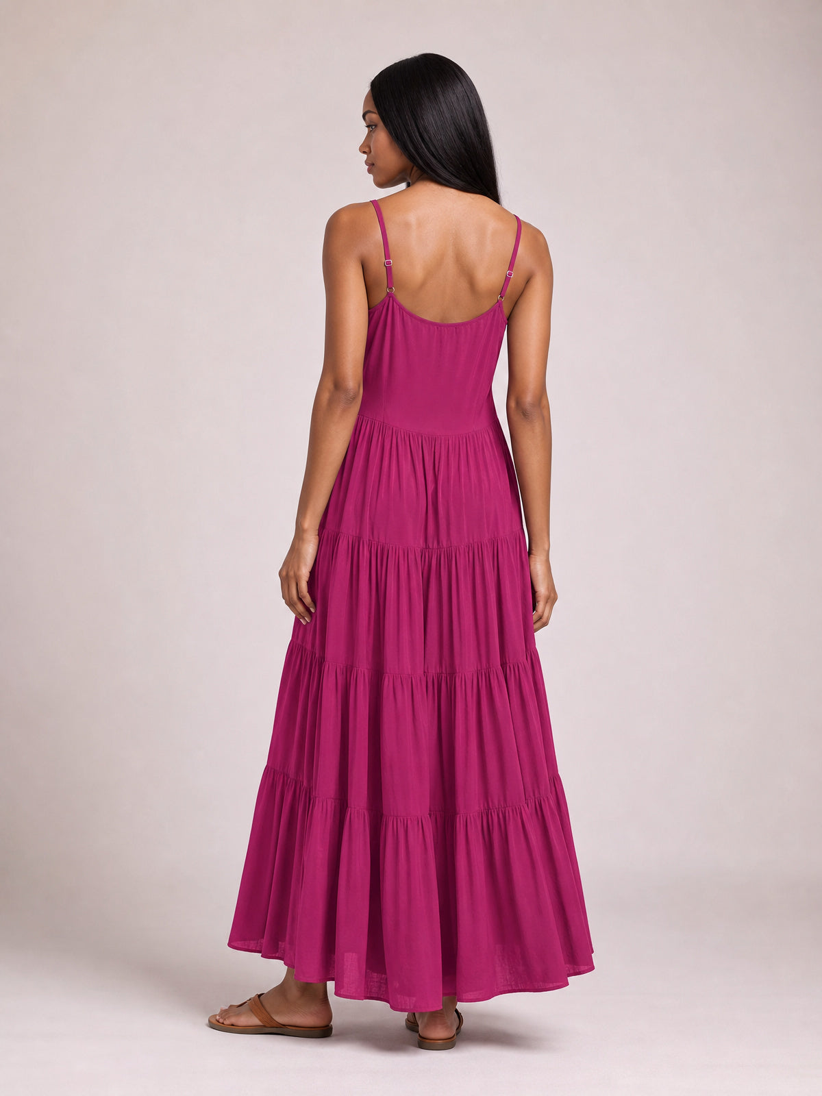 Model shown from the back in a magenta ruched tiered spaghetti strap maxi dress with a scoop back, flowing full skirt, and floor-skimming silhouette.
