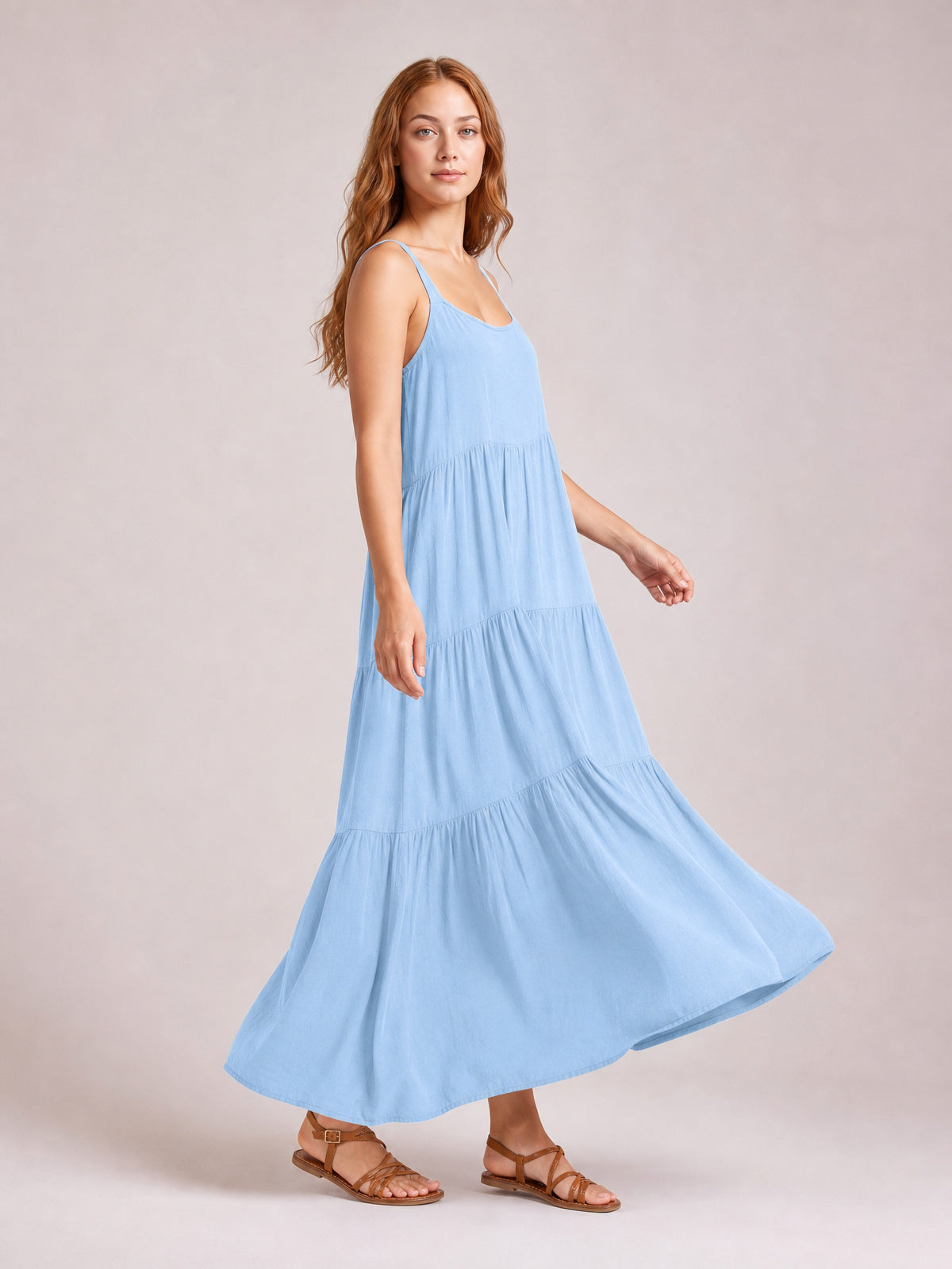 Model steps in a light blue ruched tiered maxi dress with spaghetti straps, scoop neckline, relaxed silhouette, gathered seams, and a flowing floor-length skirt.
