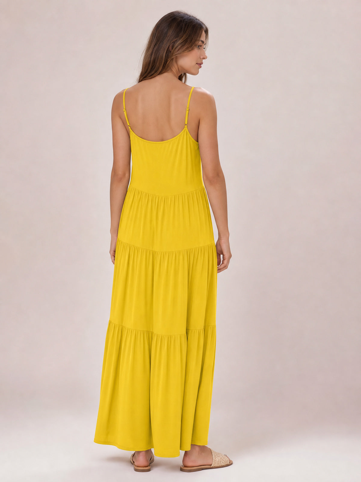 A model stands facing away in a bright yellow ruched tiered spaghetti strap maxi dress with a relaxed, flowing silhouette and gathered skirt.