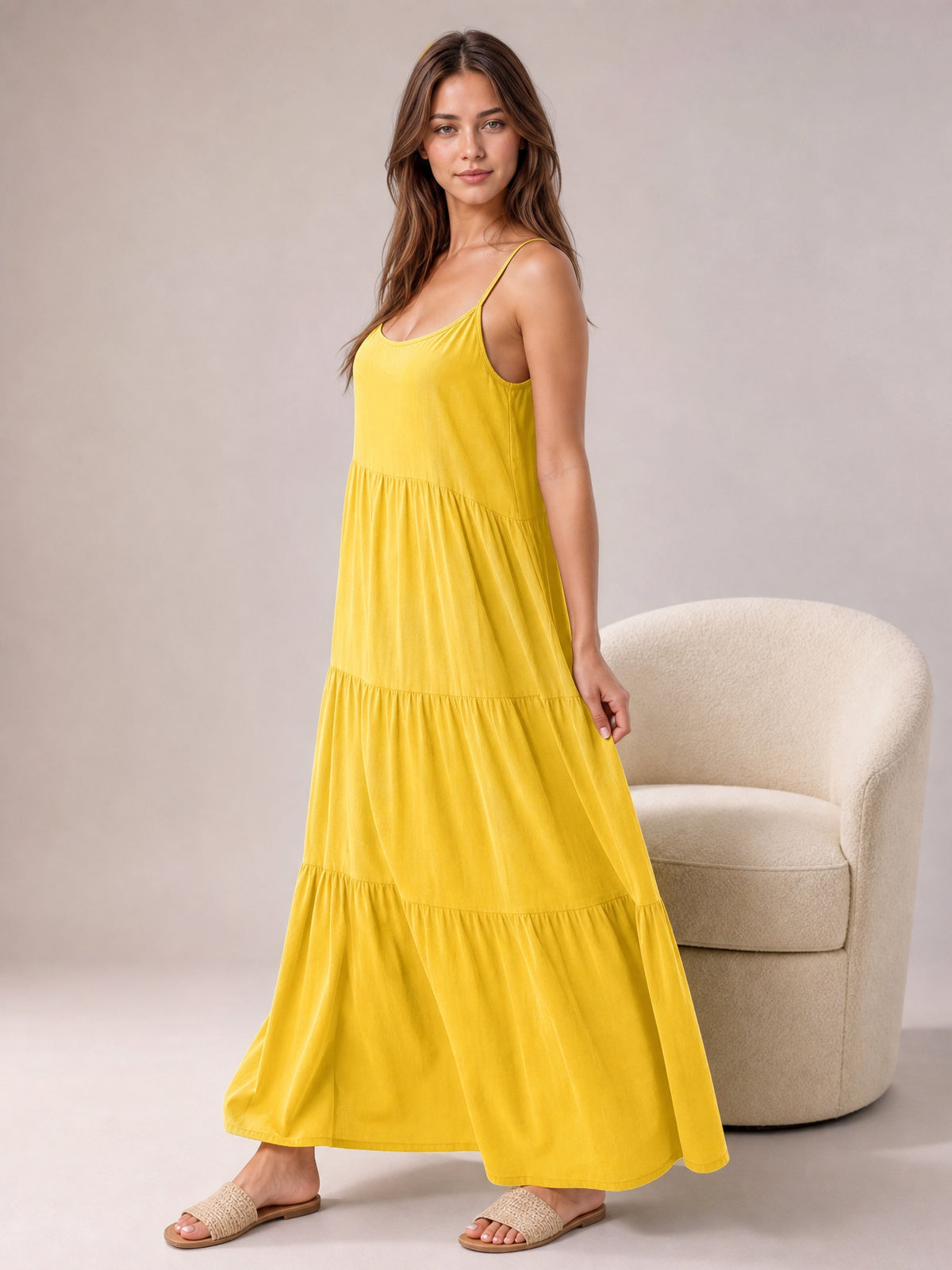 Model poses in a bright yellow ruched tiered spaghetti strap maxi dress with a scoop neckline, flowing full silhouette, and flat sandals.