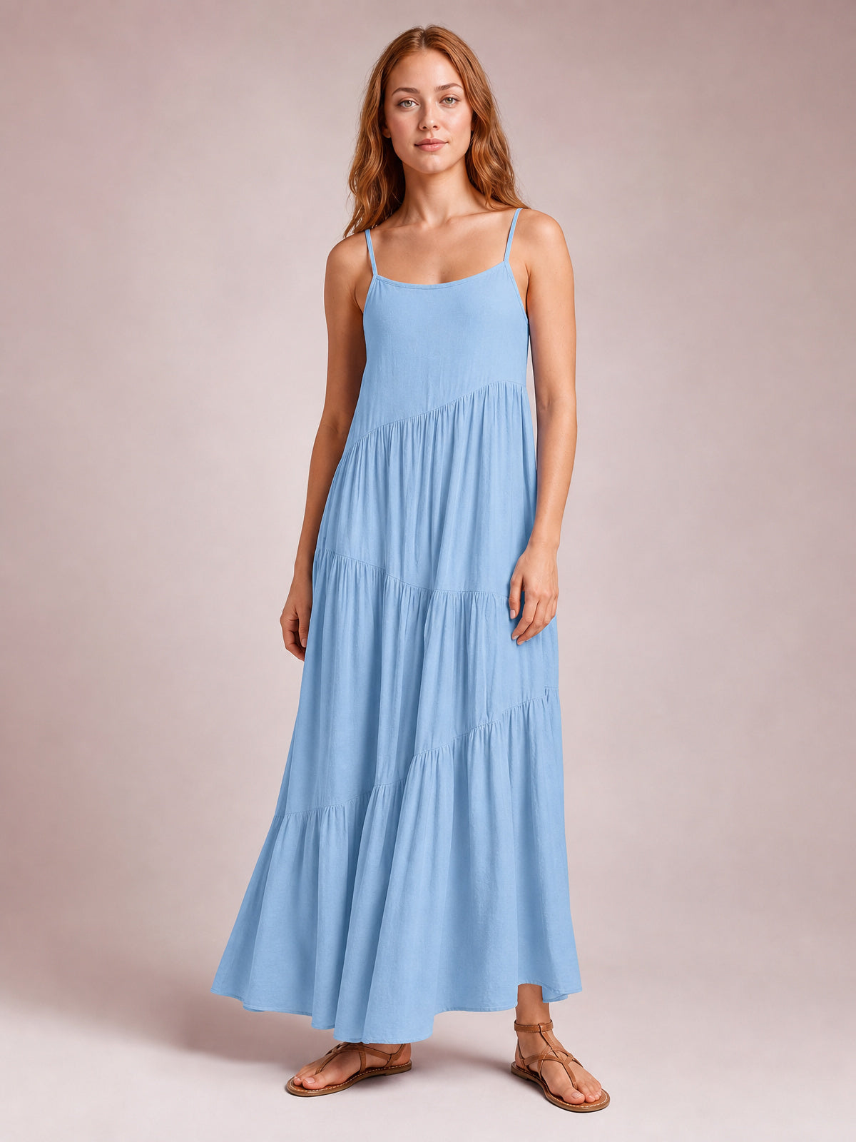 Model wearing a light blue ruched tiered spaghetti strap maxi dress with a scoop neckline and flowing floor-skimming silhouette, standing in sandals.