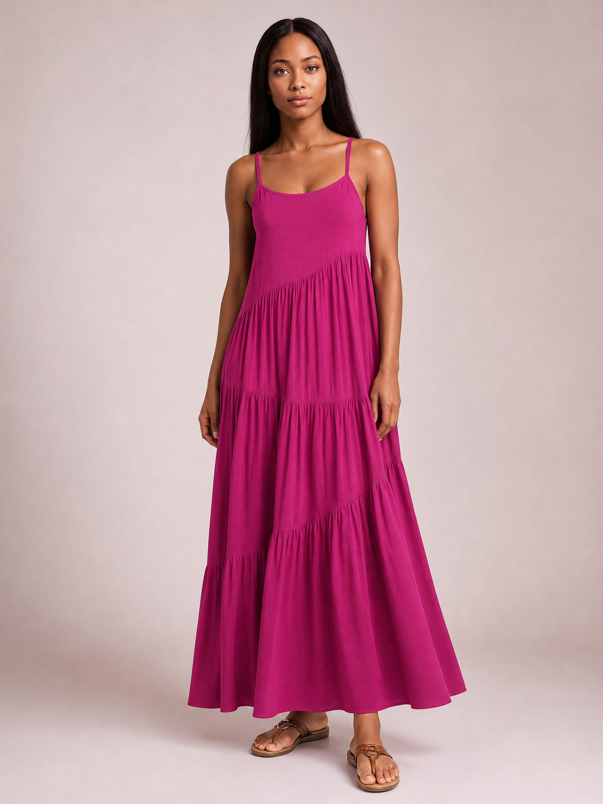 A model stands facing forward in a vivid magenta ruched tiered spaghetti strap maxi dress with a scoop neckline, gathered seams, and a flowing floor-length silhouette.
