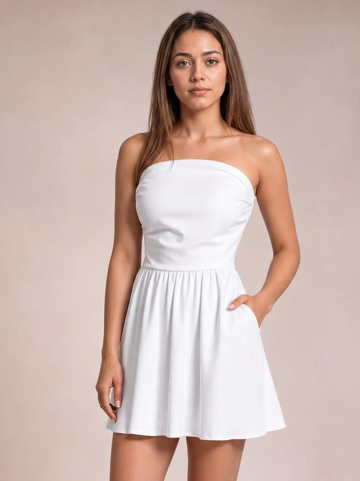 A model wears a white ruched tube mini dress with a strapless straight neckline, fitted bodice, gathered A-line skirt, and one hand in a side pocket.