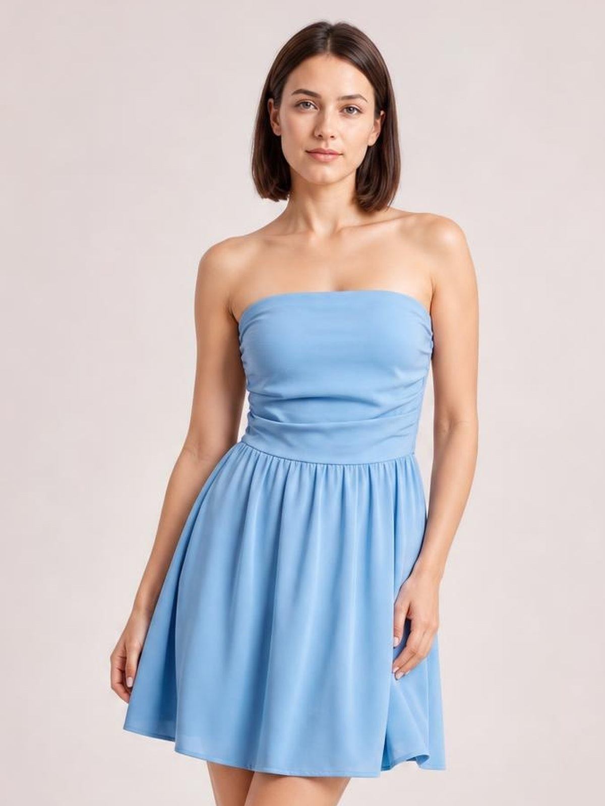 A model stands front-facing in a light blue ruched tube mini dress with a strapless bodice and softly flared skirt, hands at her sides.