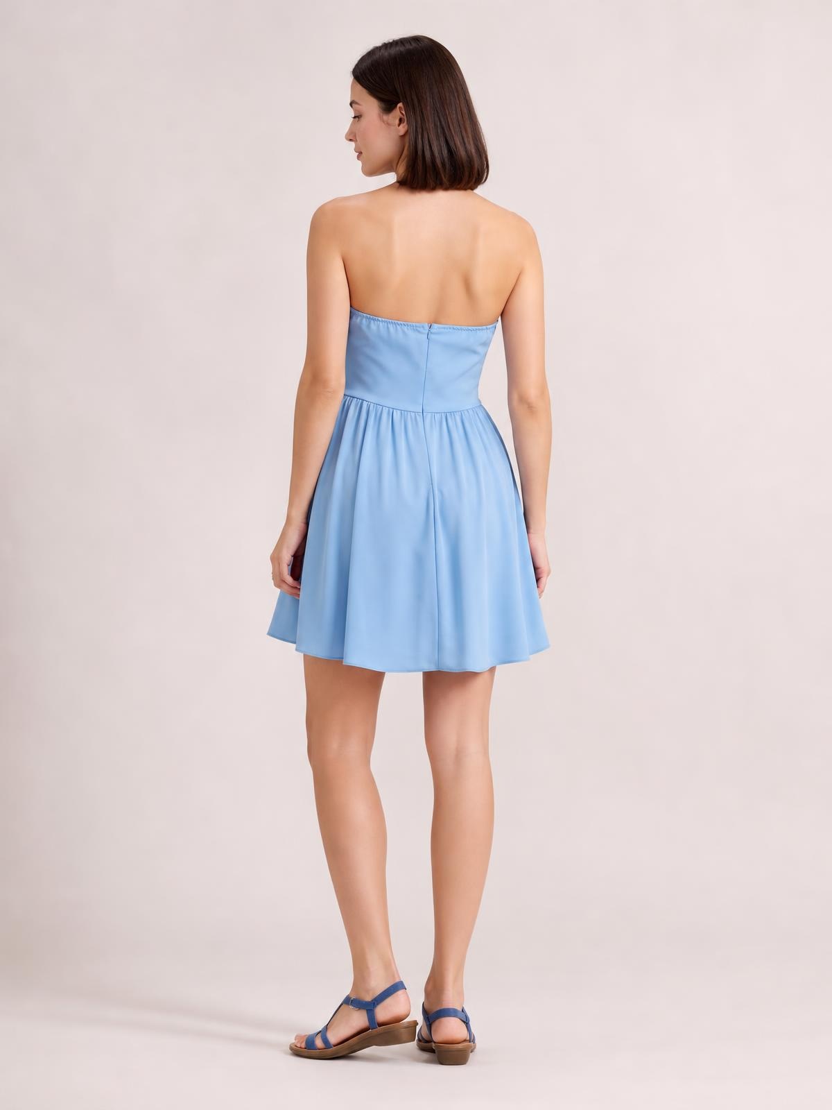 A model stands facing away in a light blue strapless mini dress with a fitted bodice, center-back seam, and gathered flared skirt.