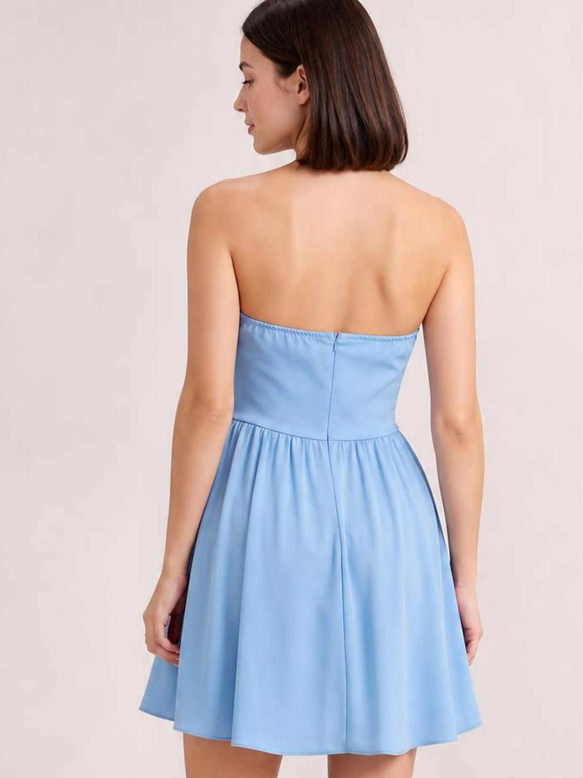 Model shown from behind in a light blue strapless mini dress with a fitted bodice, gathered waist, center-back seam, and softly flared skirt.