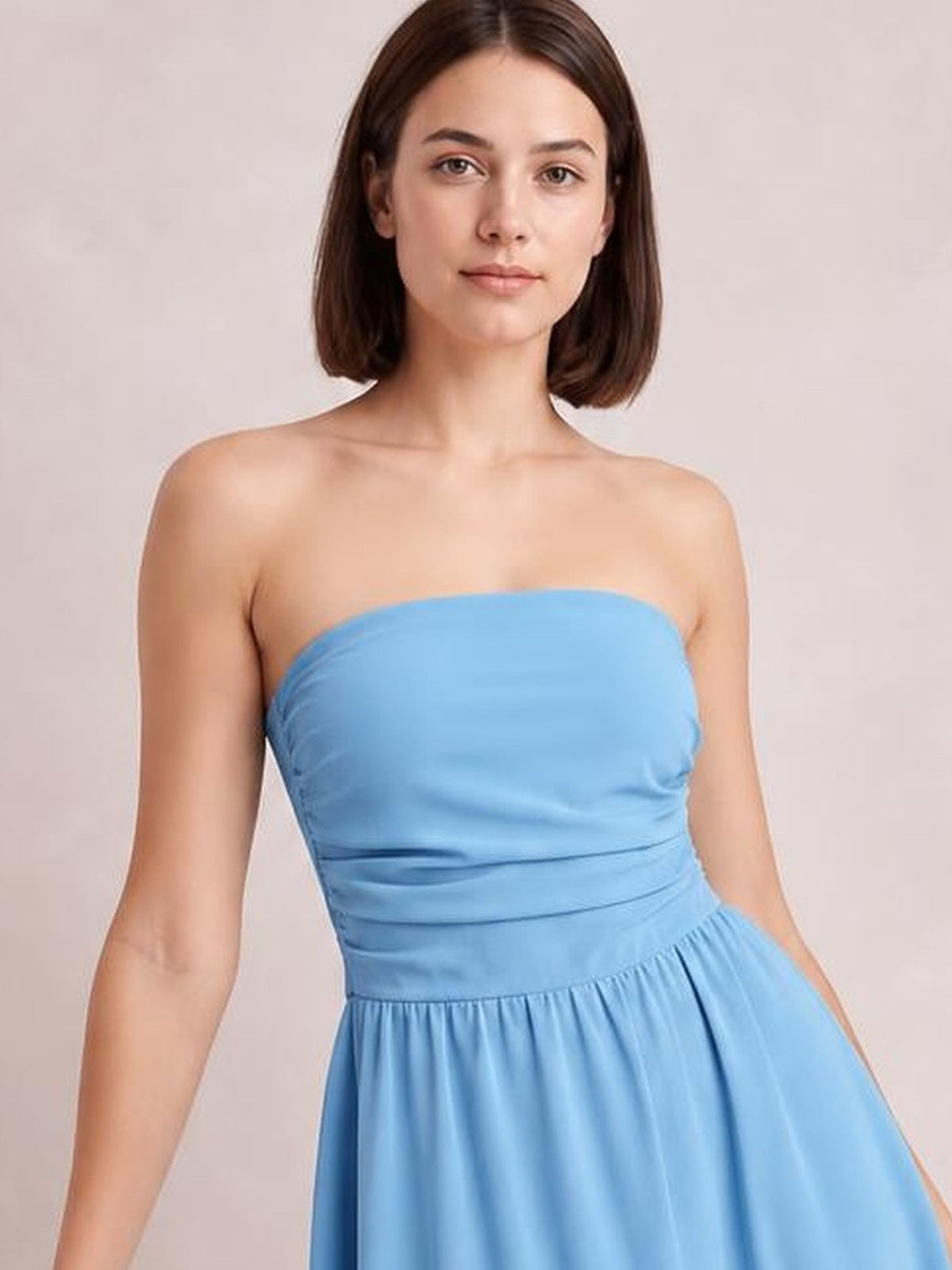 Model wears a light blue ruched tube mini dress with a strapless fitted bodice, gathered waist, and gently flared skirt, standing in a relaxed pose.