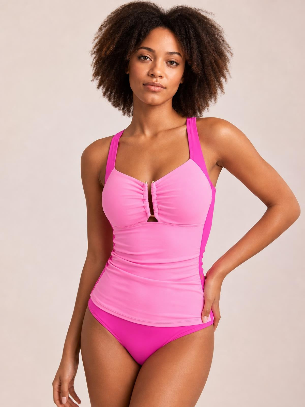 Model poses with one hand on her hip in a bright pink ruched tummy control tankini, featuring a fitted longline silhouette, wide straps, center zipper, and matching bikini bottoms.