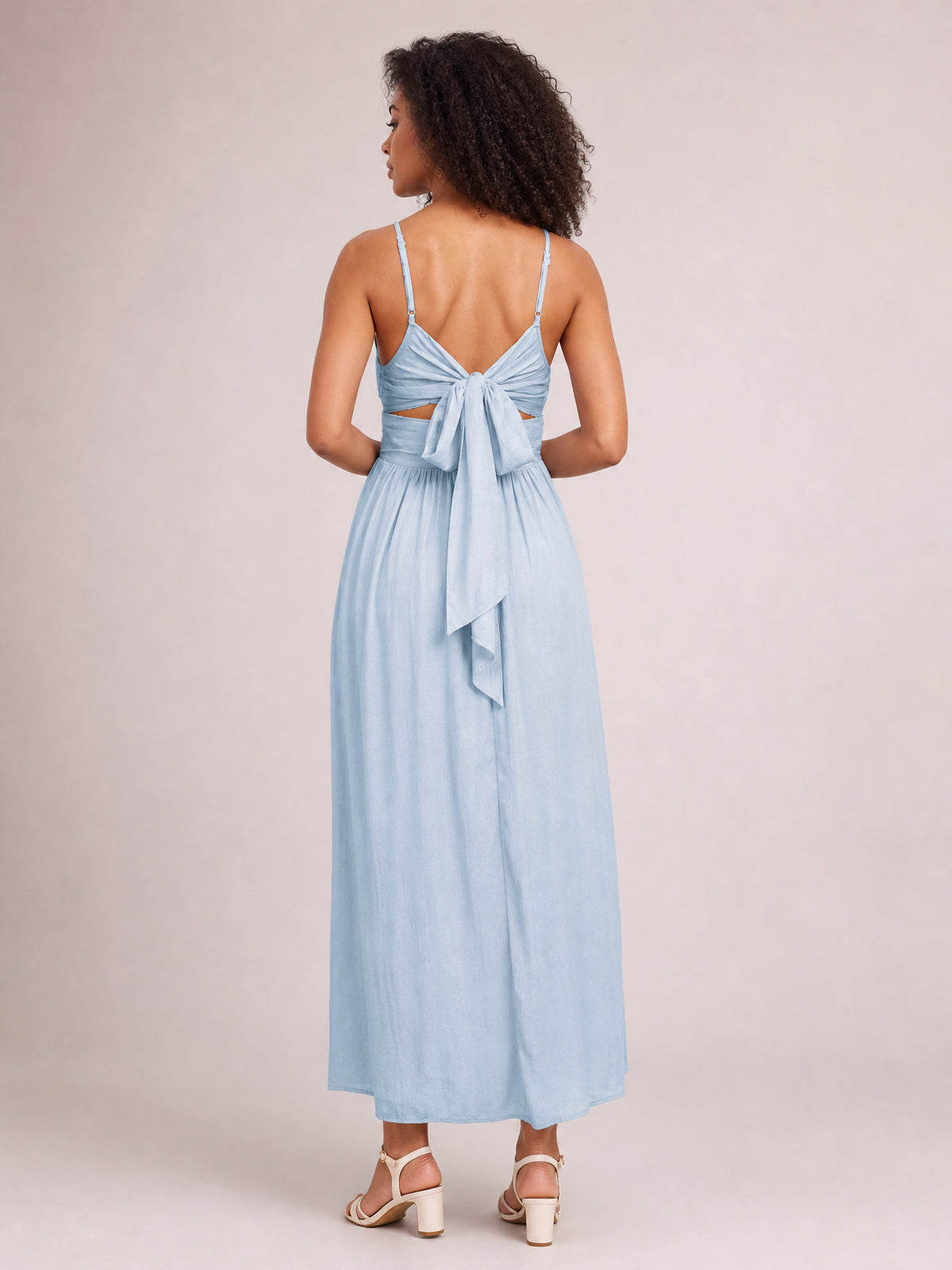 Model shown from the back in a light blue ruched cami dress with slender straps, gathered bodice, tied back detail, and a long flowing skirt.
