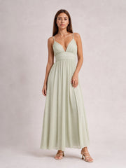 Model poses in a pale green ruched V-neck cami dress with slender straps, a defined waist, and a flowing floor-length skirt.
