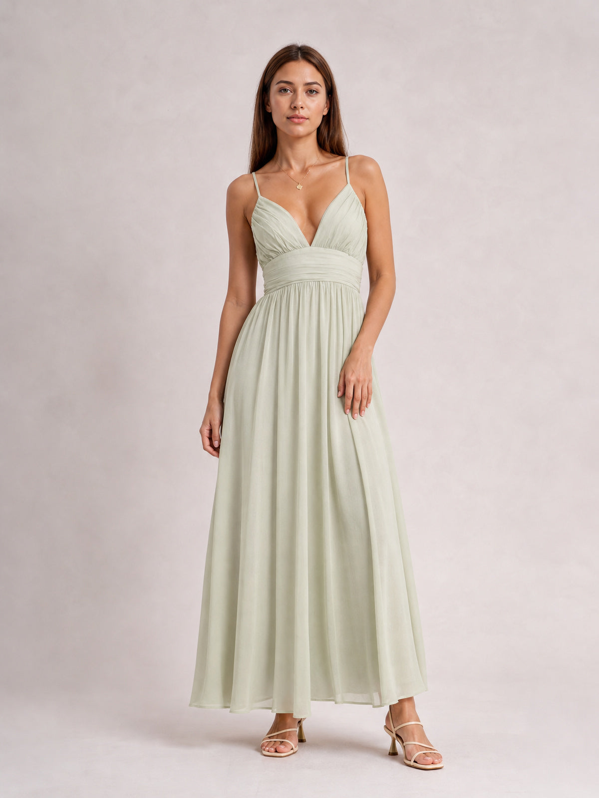 Model poses in a pale green ruched V-neck cami dress with slender straps, a defined waist, and a flowing floor-length skirt.