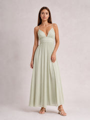 Model poses in a pale green ruched V-neck cami dress with slender straps, a defined waist, and a flowing floor-length skirt.