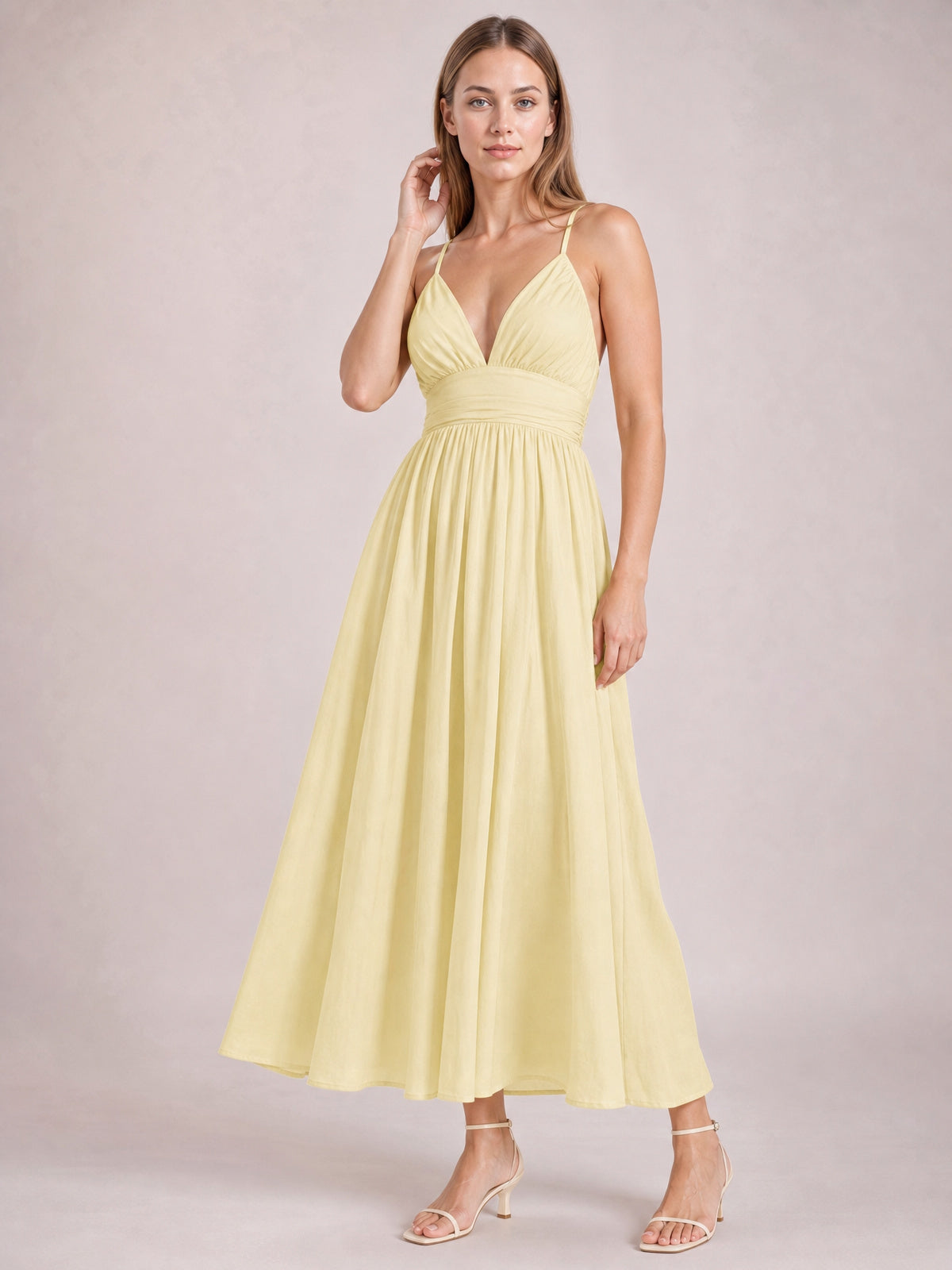A model poses in a pale yellow ruched V-neck cami dress with slender straps, a gathered waist, and a flowing long A-line skirt.