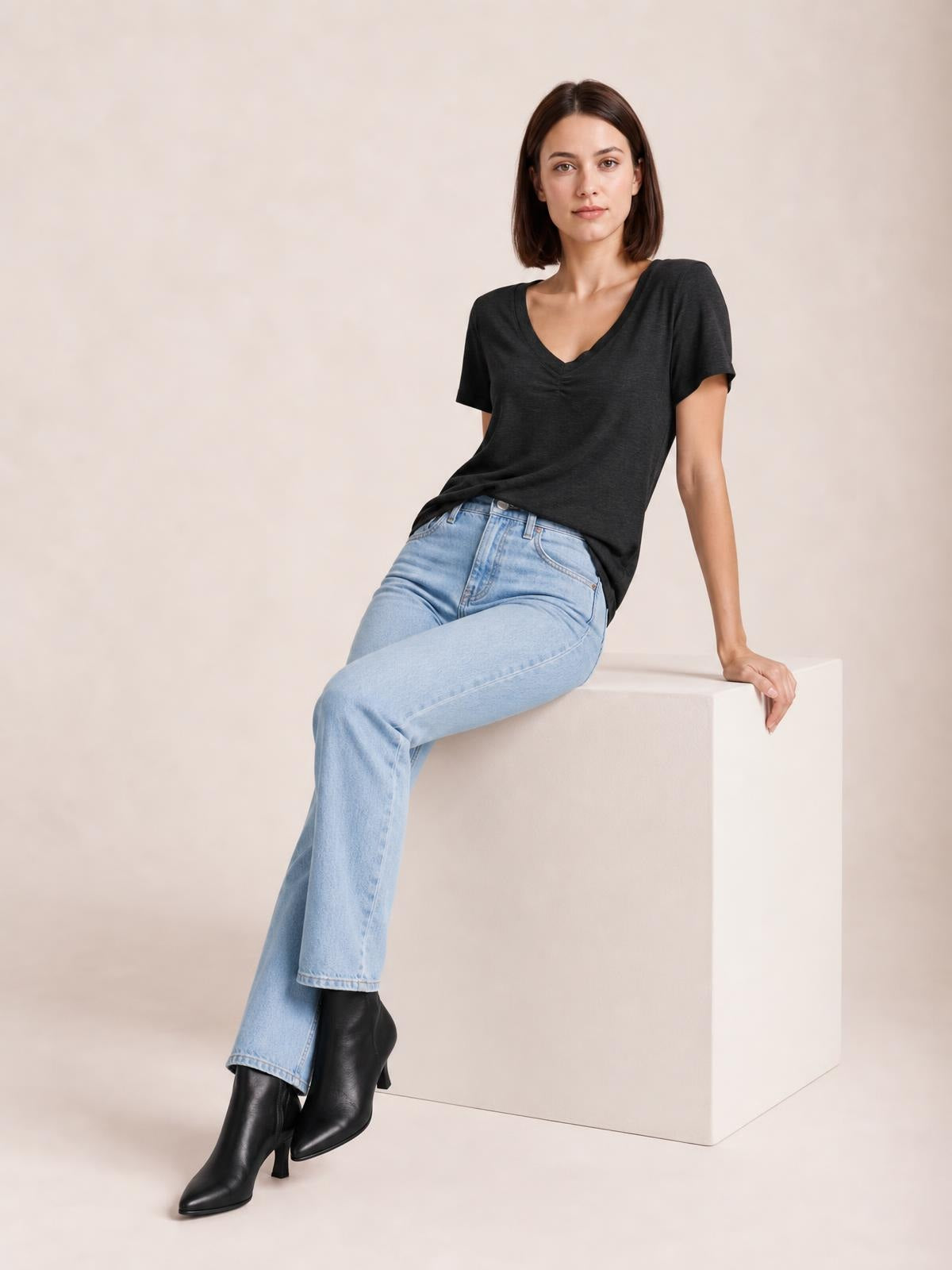 Model seated in a relaxed pose wears a charcoal ruched V-neck short sleeve T-shirt with a loose silhouette and subtle stretch.