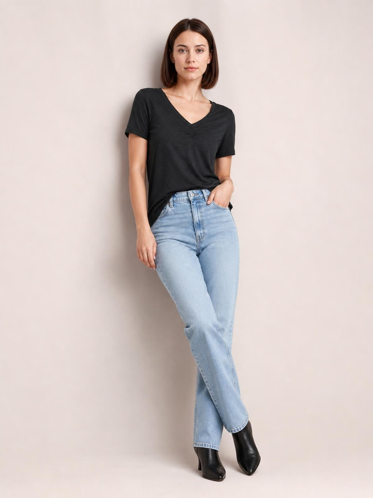 Model poses in a black ruched V-neck short sleeve T-shirt with a relaxed silhouette, paired with light-wash jeans.