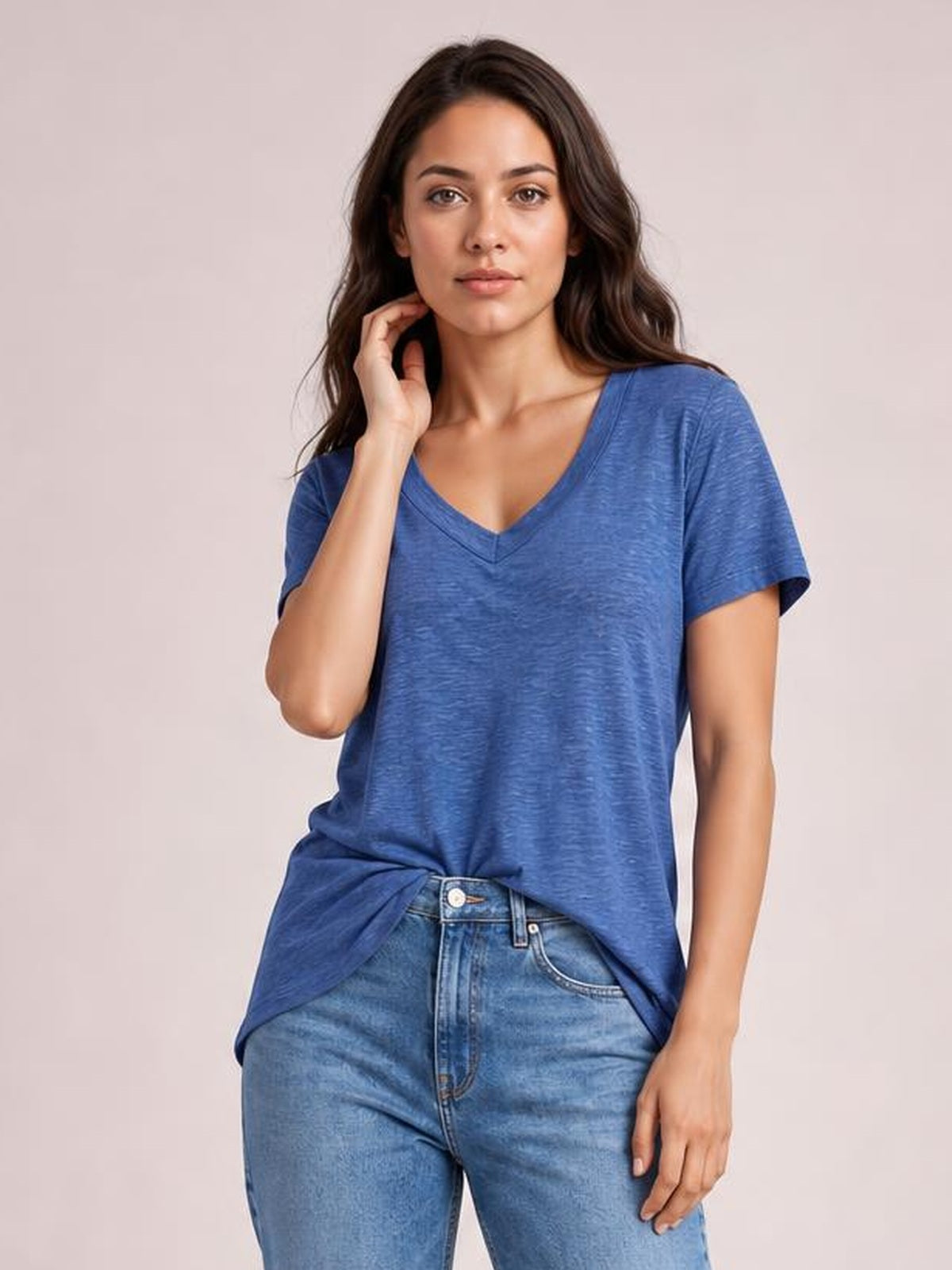 A model wears a blue ruched V-neck short-sleeve T-shirt with a relaxed silhouette and front knot, posing with one hand touching her neck.