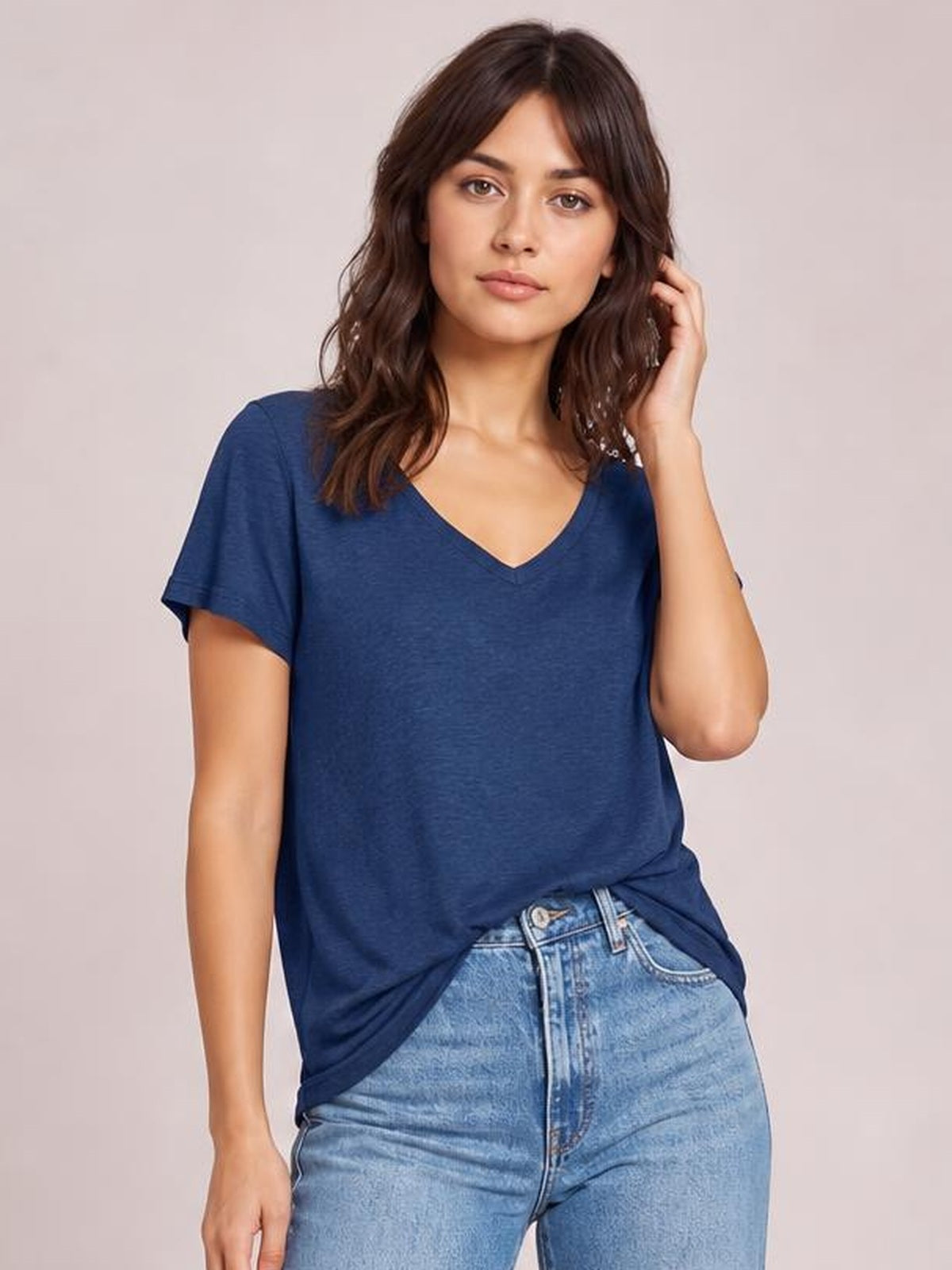 Model wearing a navy blue short-sleeve V-neck T-shirt with a relaxed silhouette, shown standing with one hand touching her hair.