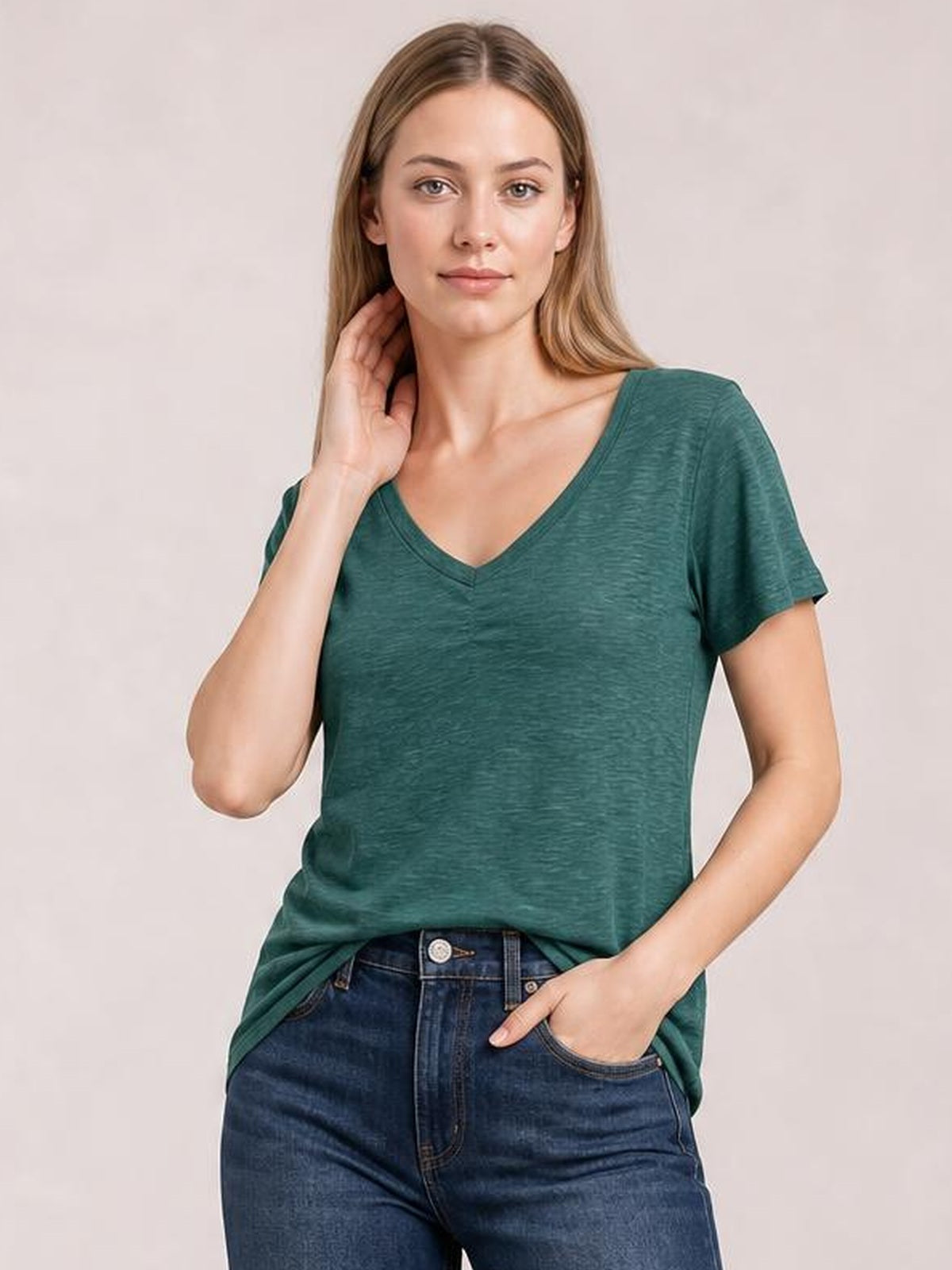 Model poses with one hand near her neck in a teal ruched V-neck short-sleeve T-shirt with a relaxed silhouette and slightly textured finish.