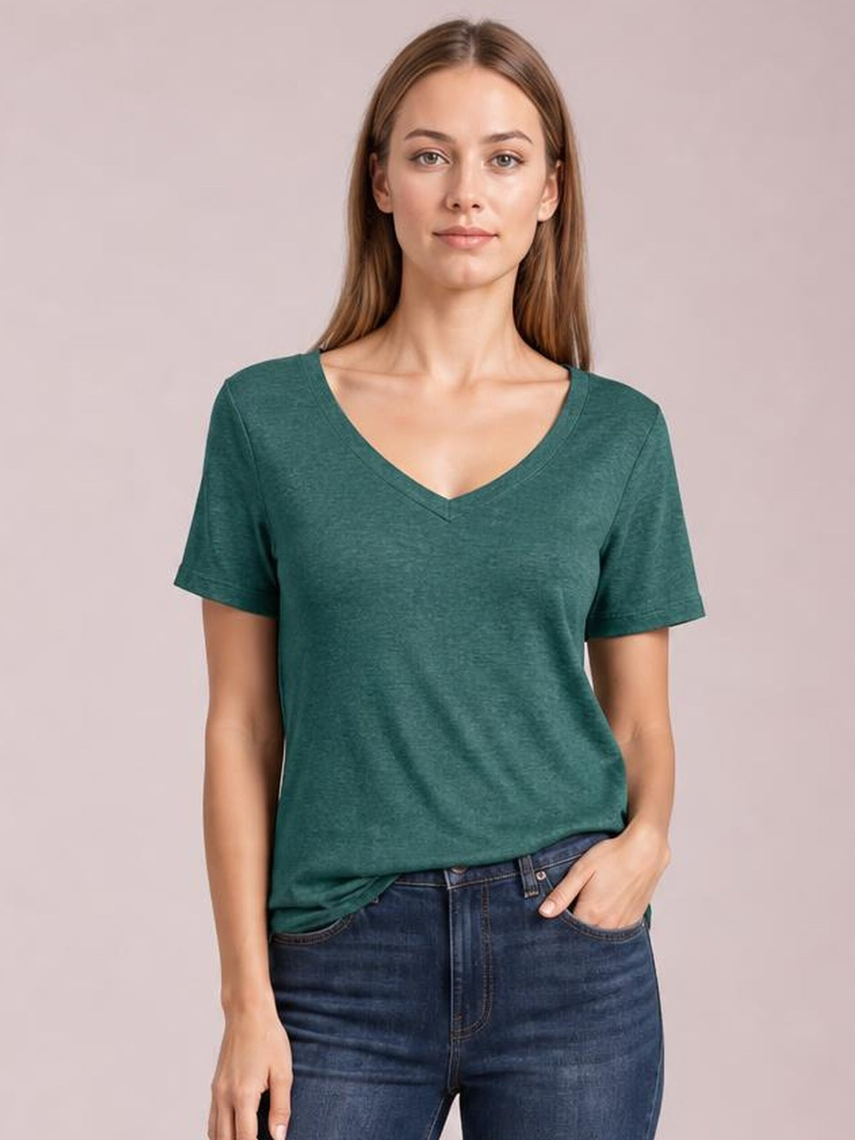 A front-facing model wears a teal green V-neck short-sleeve T-shirt with a relaxed straight silhouette and one hand resting in her jeans pocket.