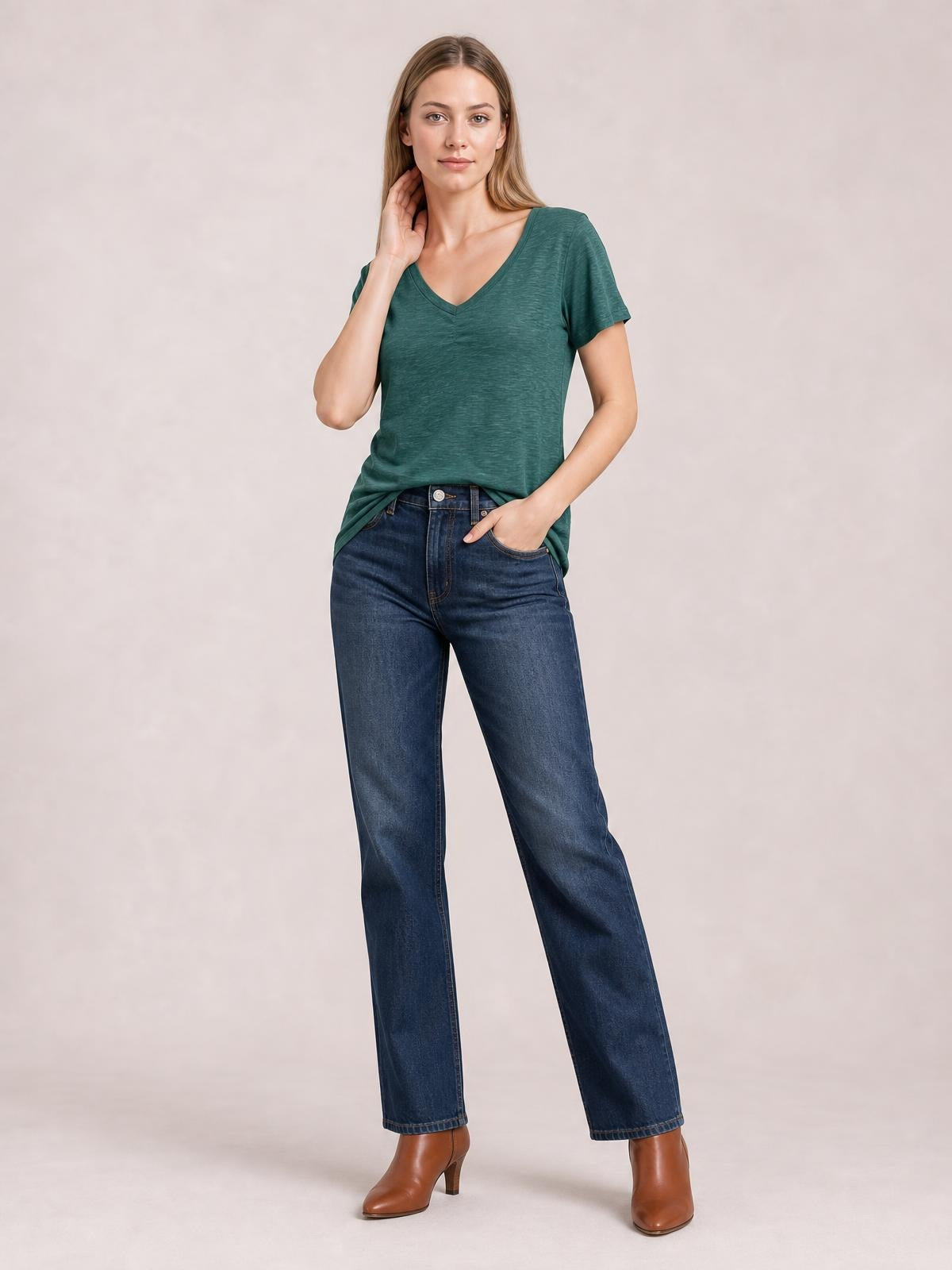 A model wears a teal ruched V-neck short sleeve T-shirt with a relaxed straight silhouette, standing with one hand at her neck and the other in her pocket.