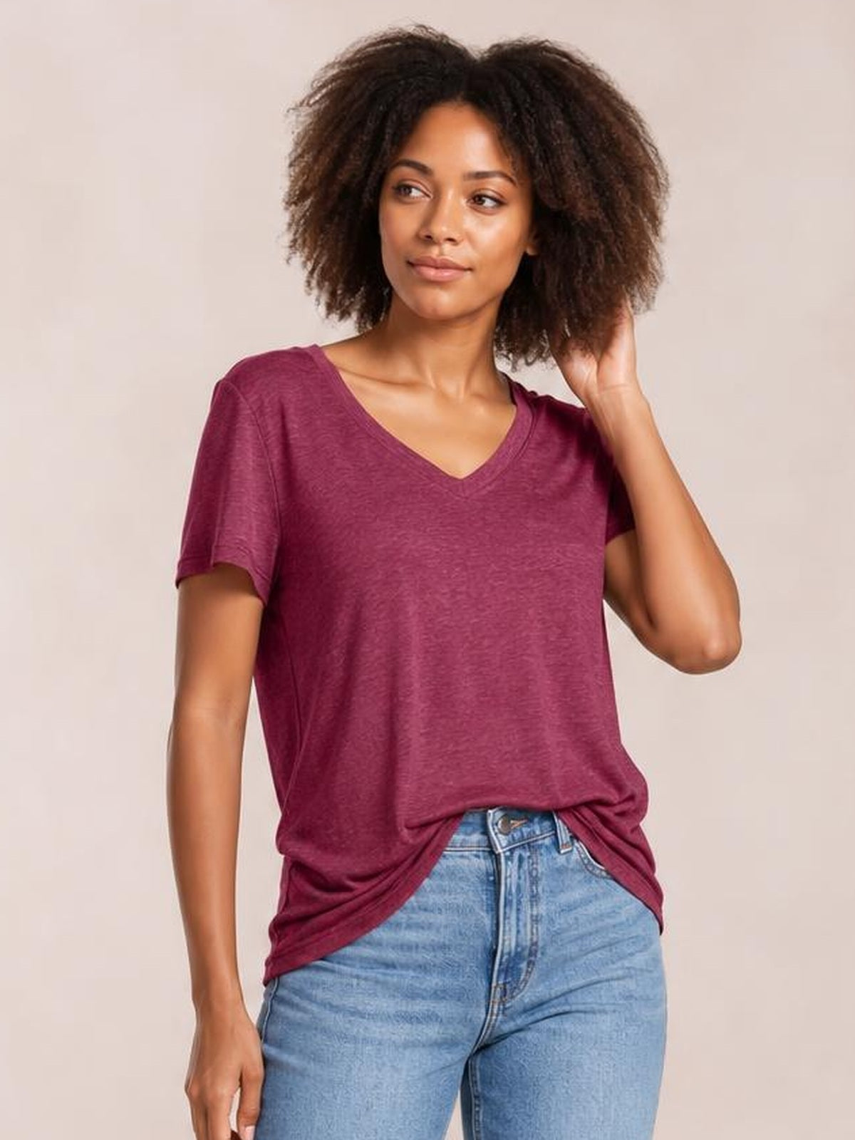 Model wearing a burgundy ruched V-neck short-sleeve T-shirt with a relaxed silhouette, draped hem, and slight stretch, posing with one hand in her hair.