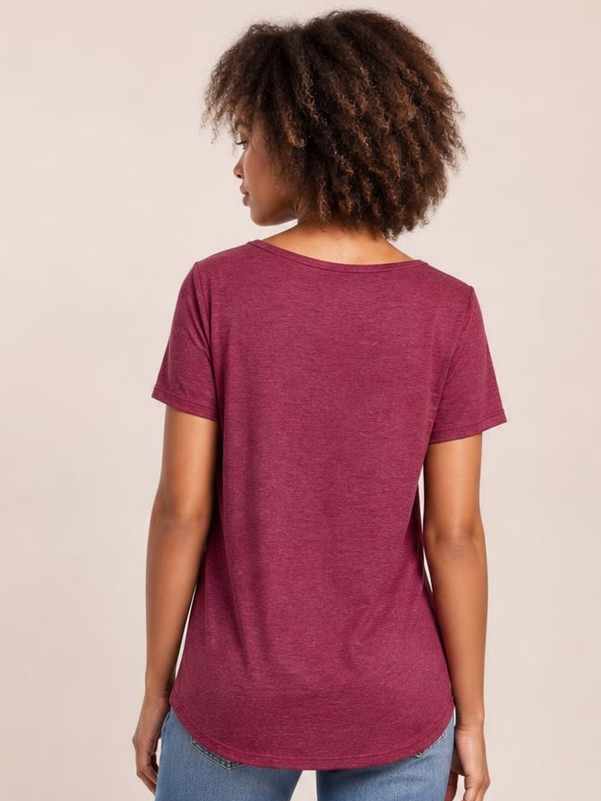 Model shown from behind wearing a burgundy short-sleeve T-shirt with a relaxed silhouette, smooth construction, and rounded hem over blue jeans.