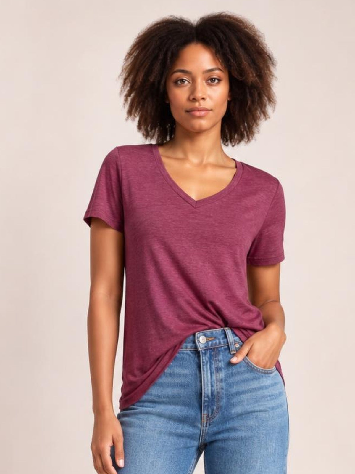 Model wearing a burgundy ruched V-neck short sleeve T-shirt with a relaxed silhouette, shown front-facing with one hand in her jeans pocket.