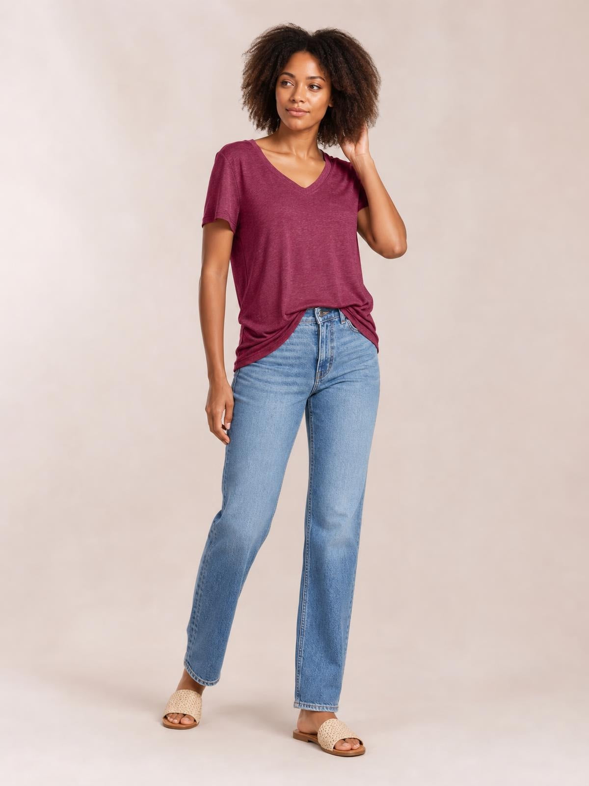 Model poses in a burgundy ruched V-neck short-sleeve T-shirt with a relaxed silhouette and softly gathered hem, paired with light-wash jeans.
