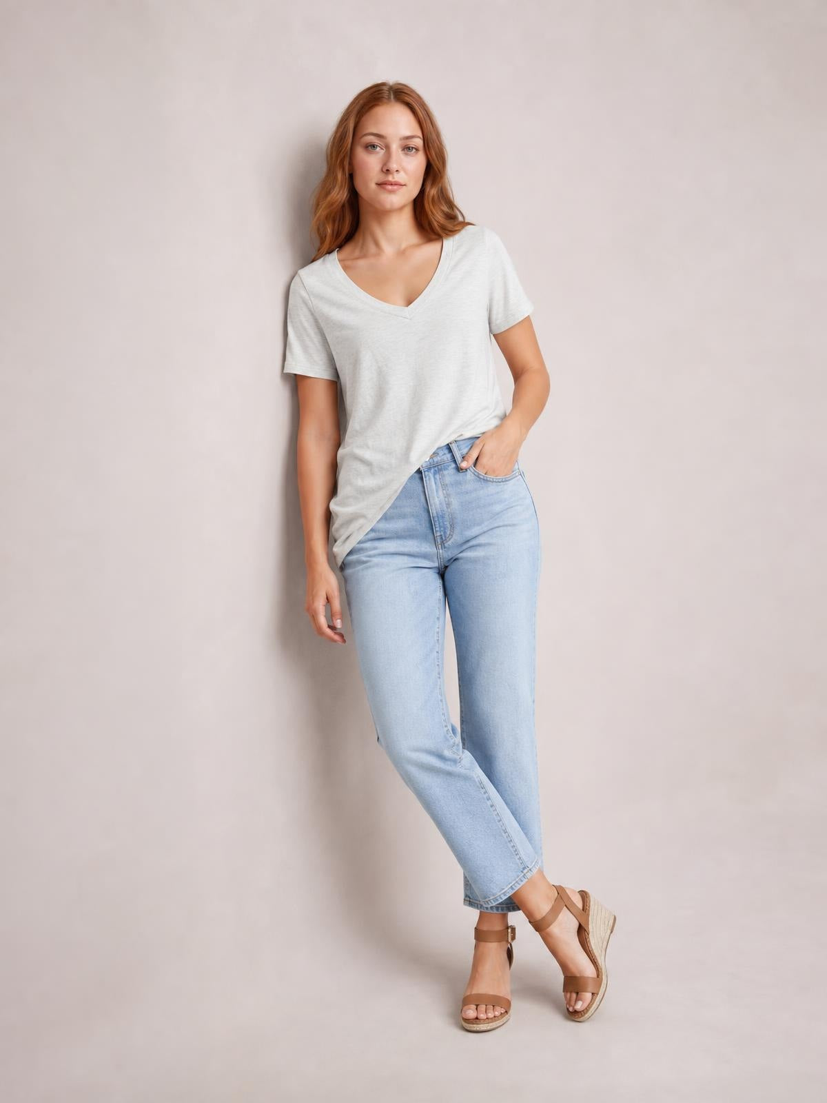 A woman models a light gray V-neck short-sleeve T-shirt with a relaxed straight silhouette, standing with one hand in her jeans pocket.