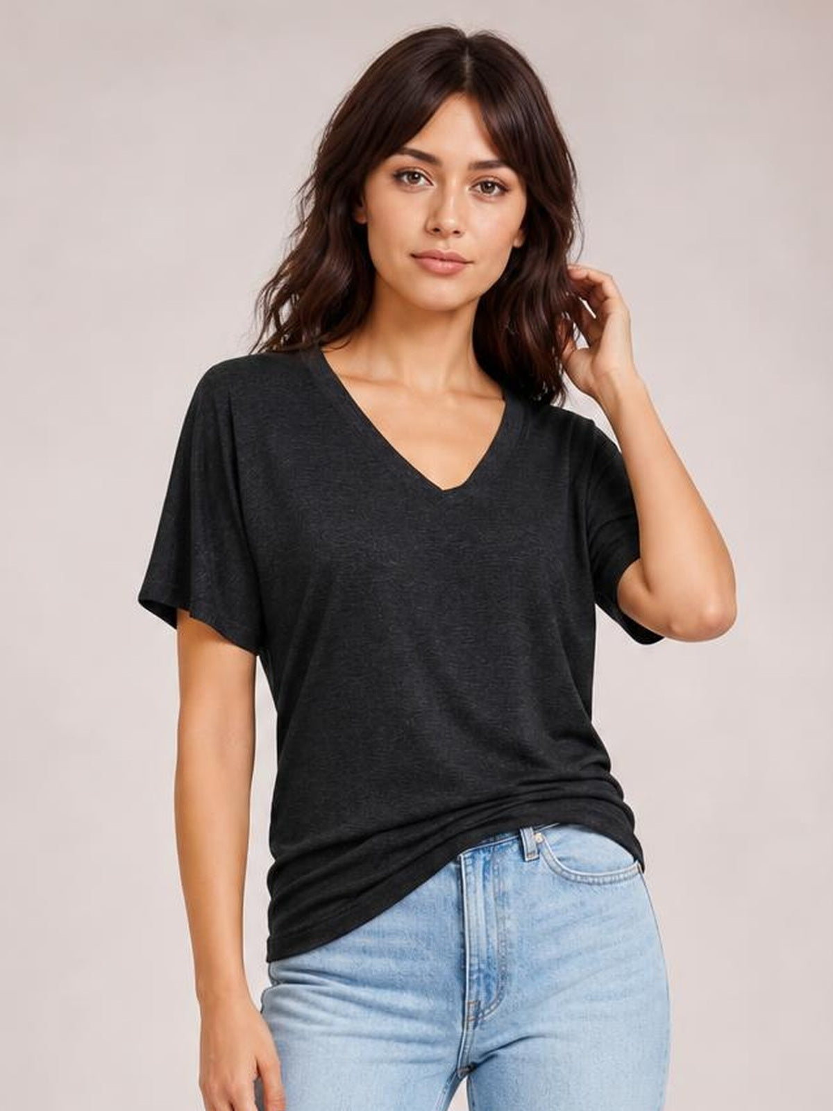 Model wears a dark charcoal short-sleeve V-neck T-shirt with a relaxed, draped silhouette and longline hem, posing with one hand in her hair.