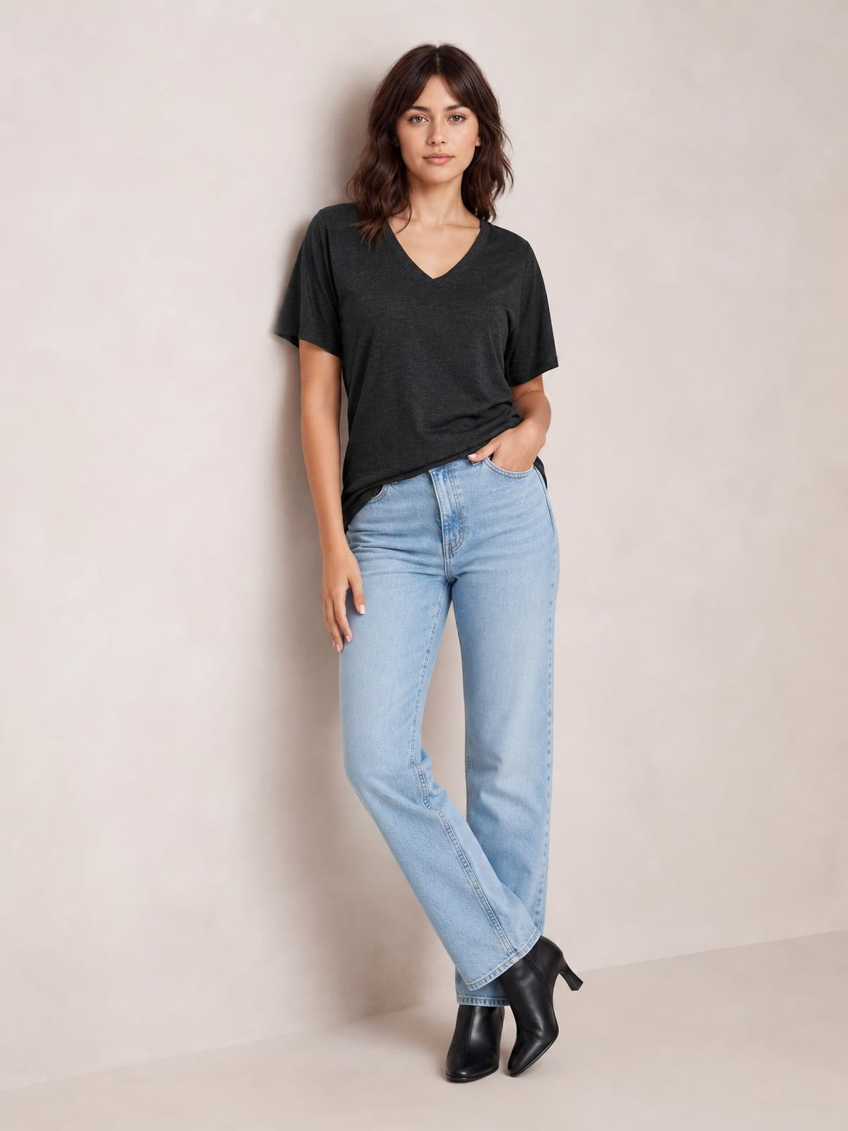 Model poses with crossed legs in a charcoal ruched V-neck short sleeve T-shirt featuring a relaxed silhouette and soft, stretchy drape.