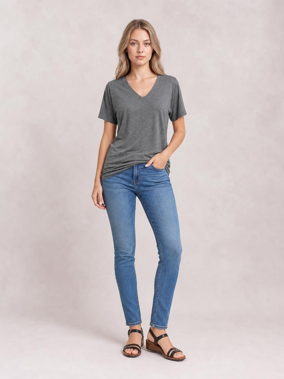 A model stands in a gray ruched V-neck short sleeve T-shirt with a relaxed silhouette, paired with jeans and one hand tucked into a pocket.