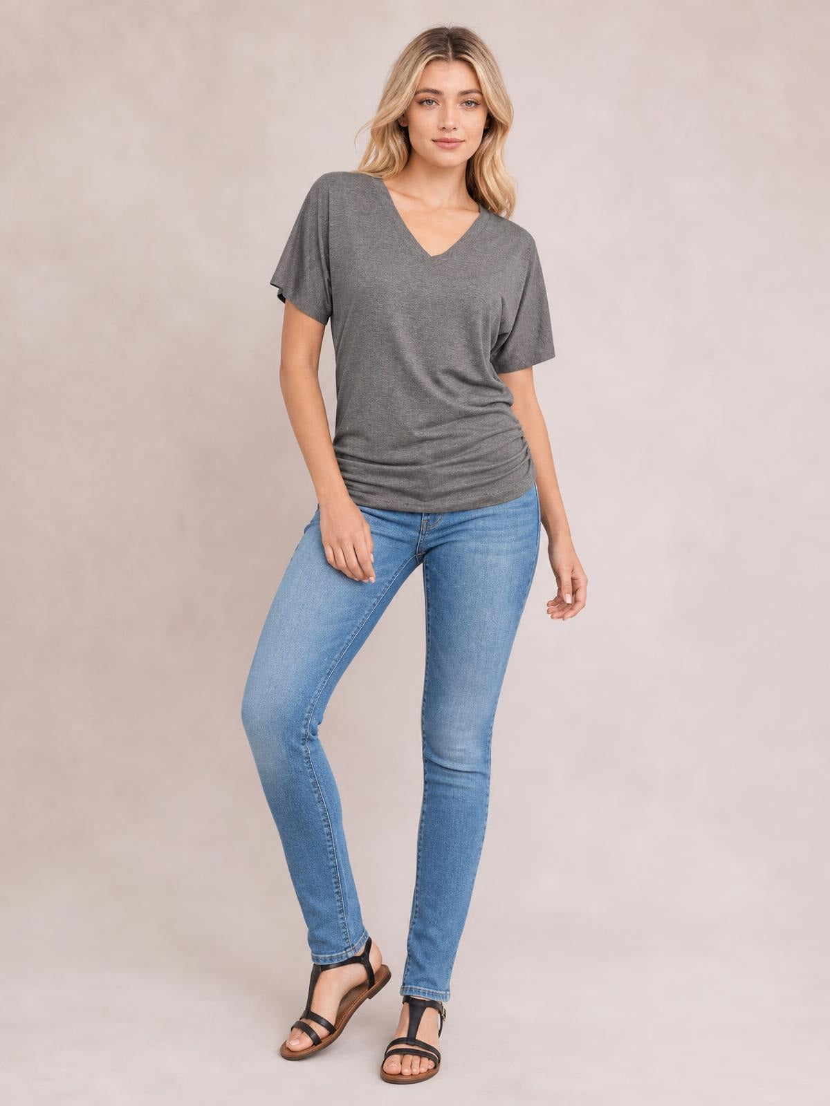 Model poses in a gray ruched V-neck short sleeve T-shirt with a relaxed silhouette and gathered detailing along the sides and hem.