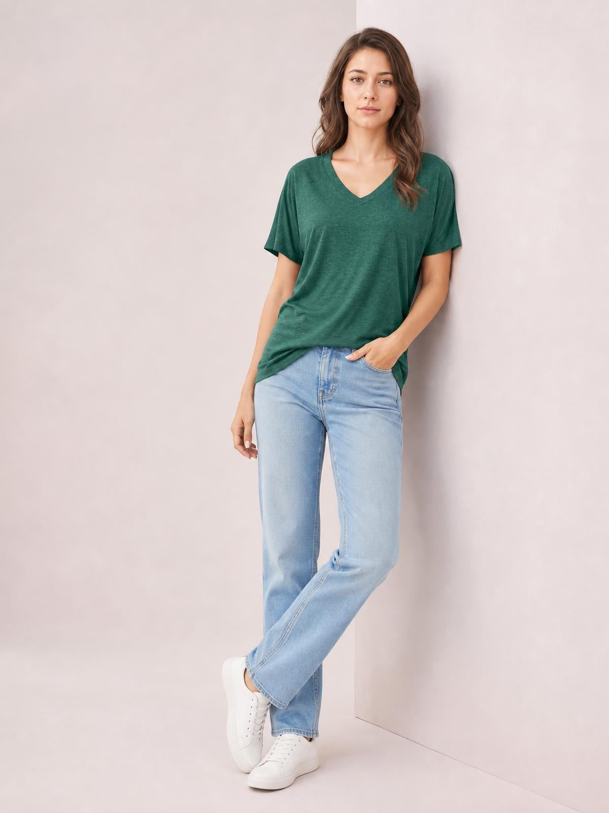 Model wears a forest green ruched V-neck short sleeve T-shirt with a relaxed silhouette, paired with light-wash jeans in a casual crossed-leg pose.