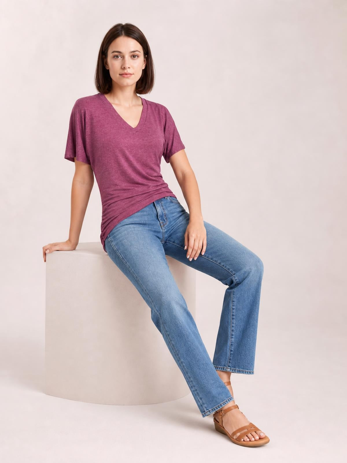 A model sits leaning on a cube in a berry Ruched V-Neck Short Sleeve T-Shirt with soft ruching, a fitted silhouette, and a curved hem.