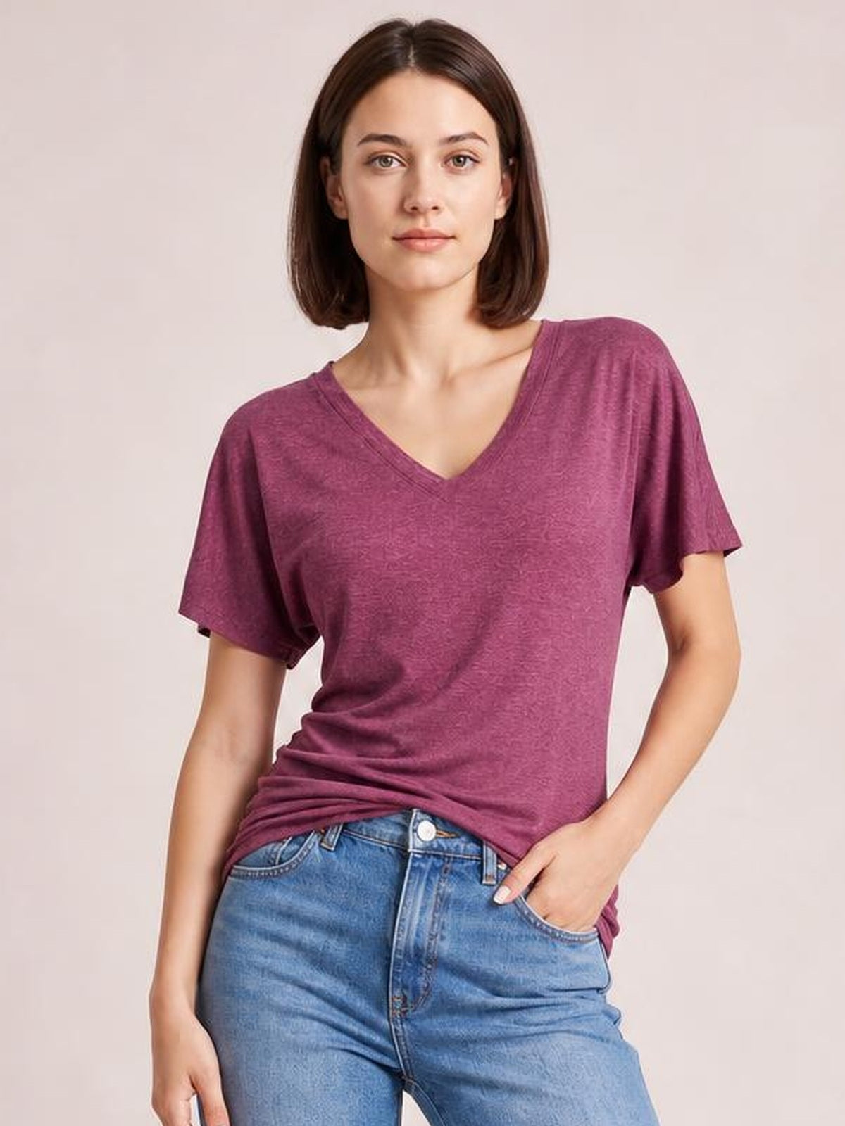 Model wearing a plum ruched V-neck short sleeve T-shirt with a relaxed, stretchy silhouette, standing with one hand in her jeans pocket.
