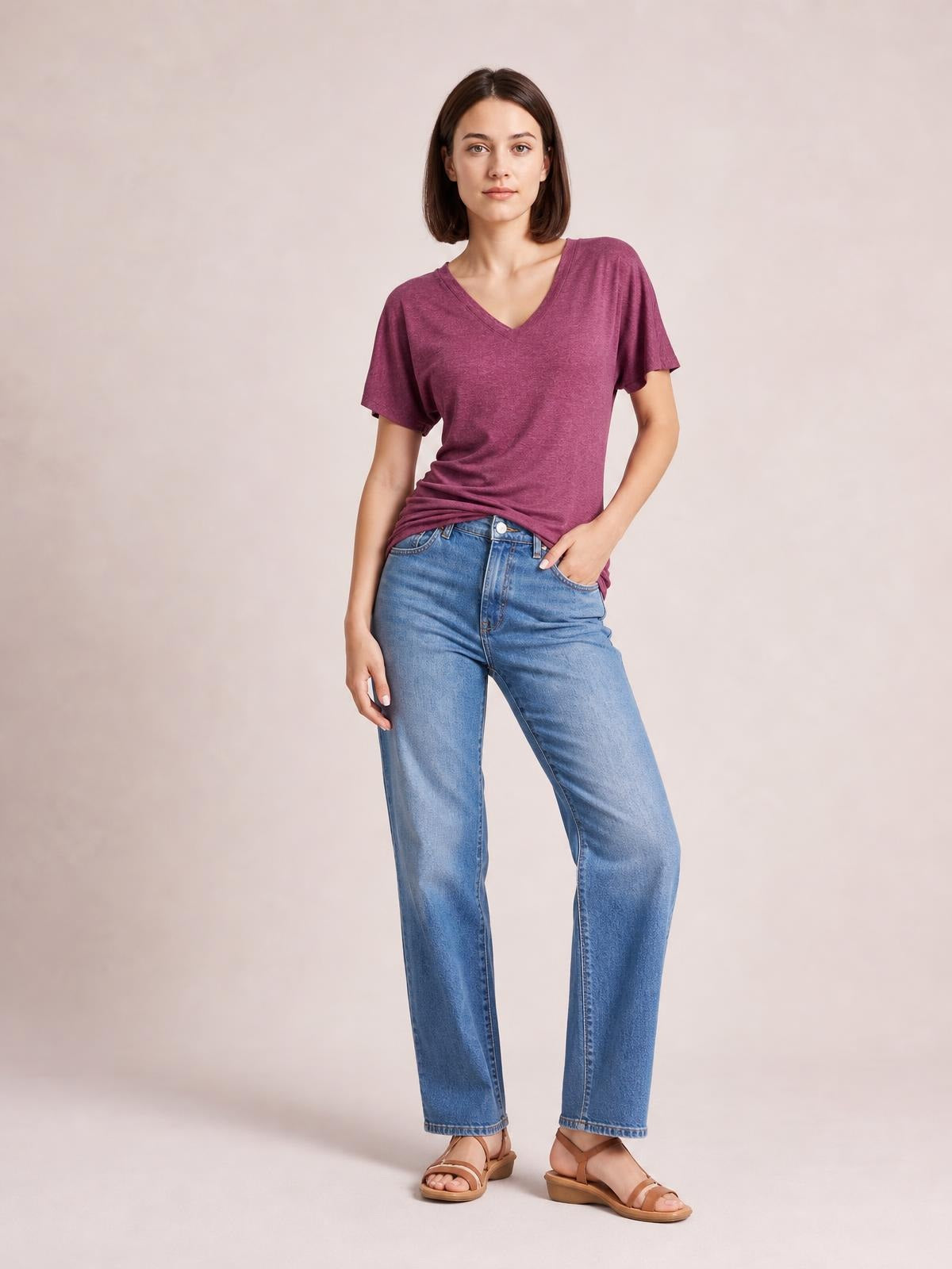 Model wears a burgundy ruched V-neck short sleeve T-shirt with a relaxed silhouette and visible side gathering, paired with jeans in a casual hand-in-pocket pose.