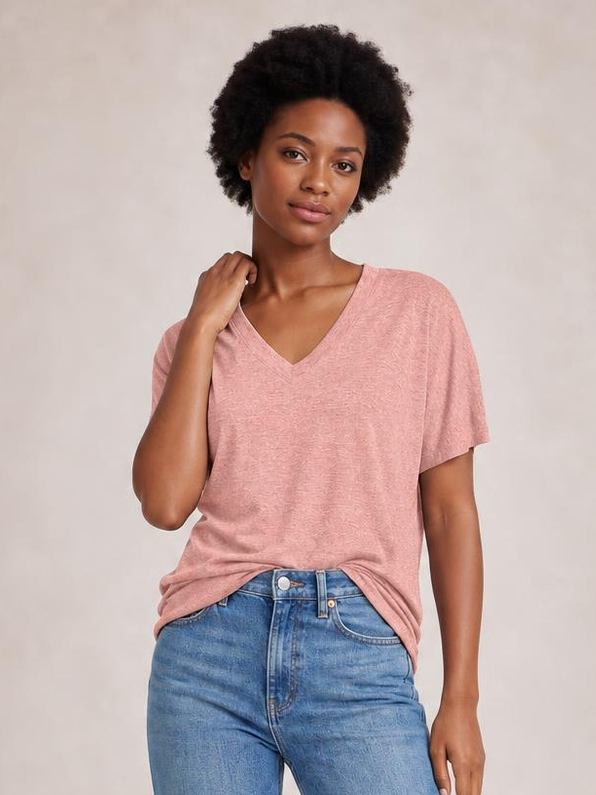 Model poses in a pink ruched V-neck short sleeve T-shirt with a relaxed silhouette, gently holding the neckline near her shoulder.