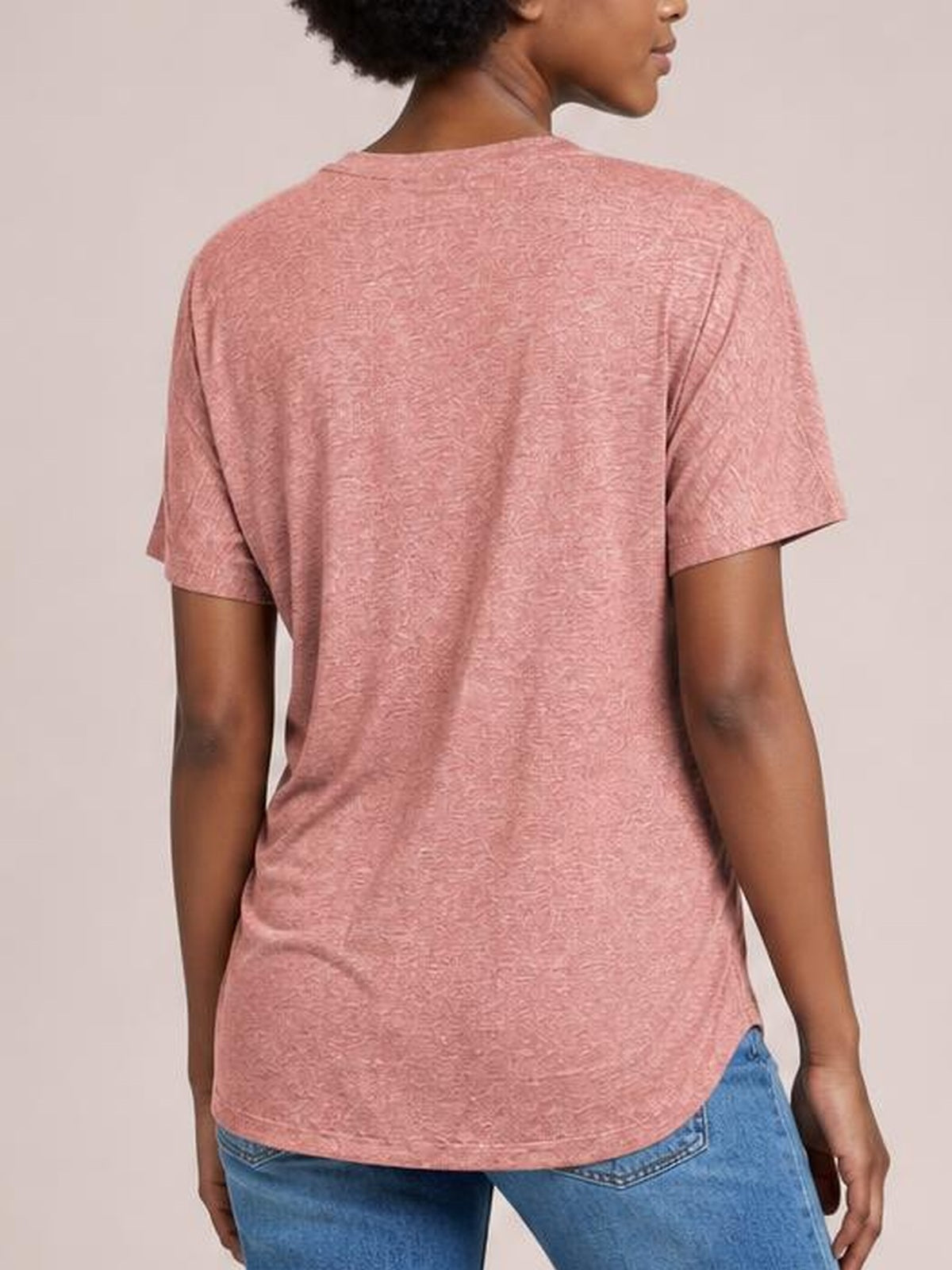 Model shown from behind wearing a dusty pink short-sleeve T-shirt with a relaxed silhouette, subtle textured pattern, and gently curved hem.