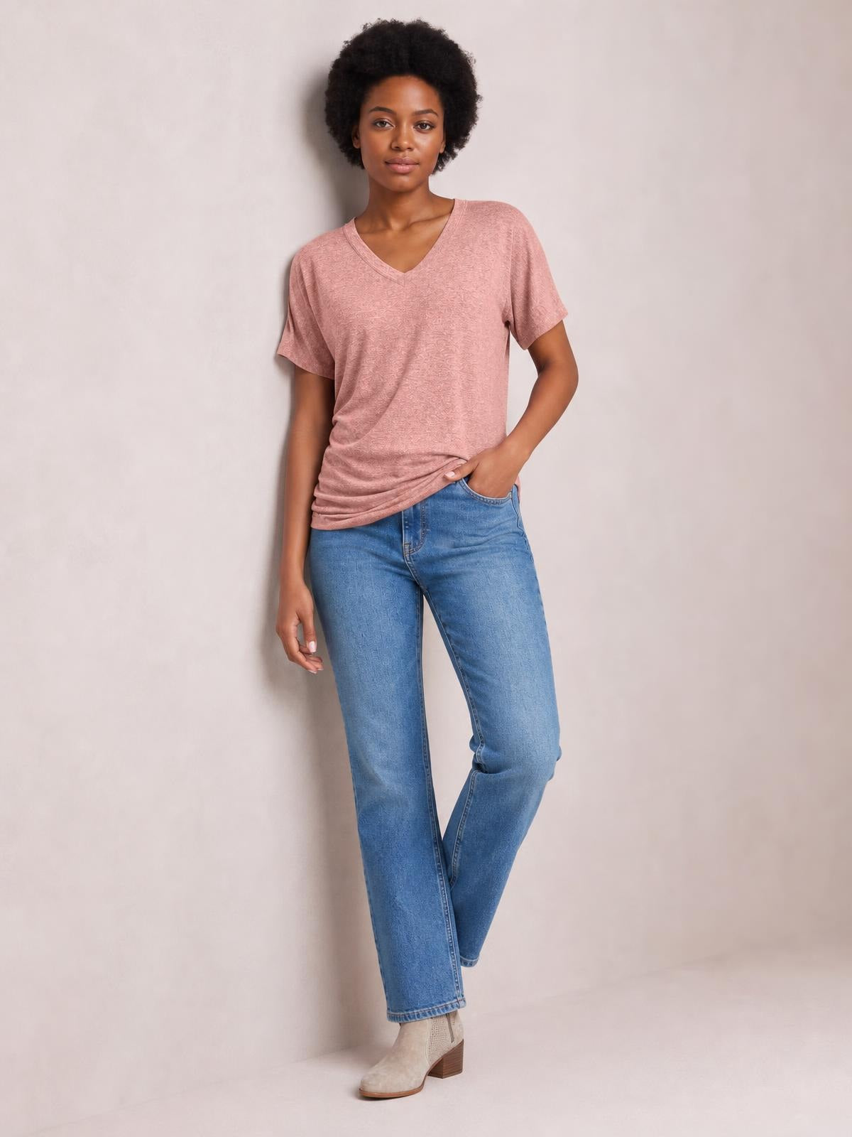 Model poses in a soft pink ruched V-neck short sleeve T-shirt with a relaxed silhouette and gathered hem, paired with blue jeans.