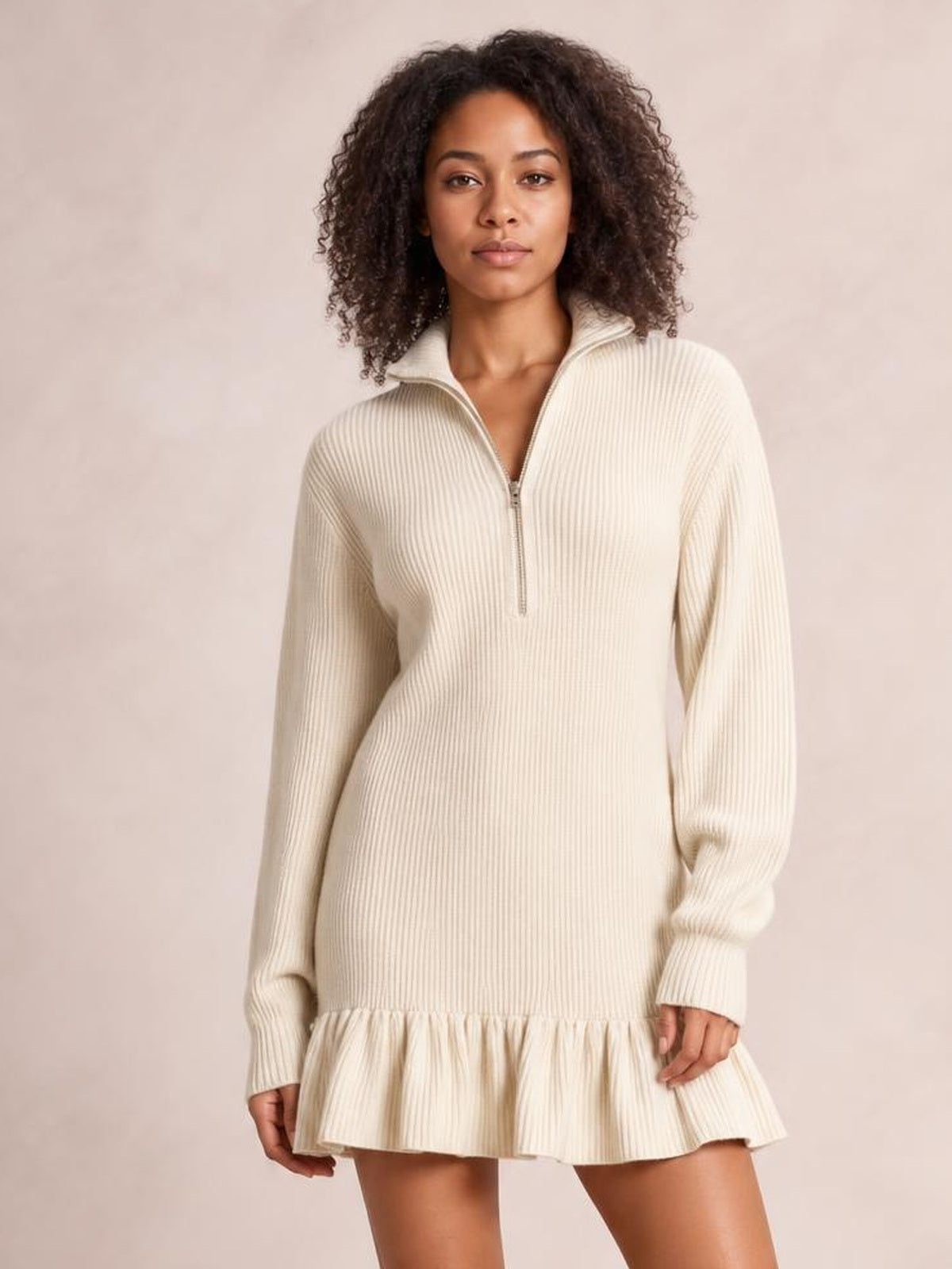 Model in a relaxed stance wears a cream ribbed dress with long sleeves, a half-zip mock neck, straight silhouette, and gathered ruffle hem.