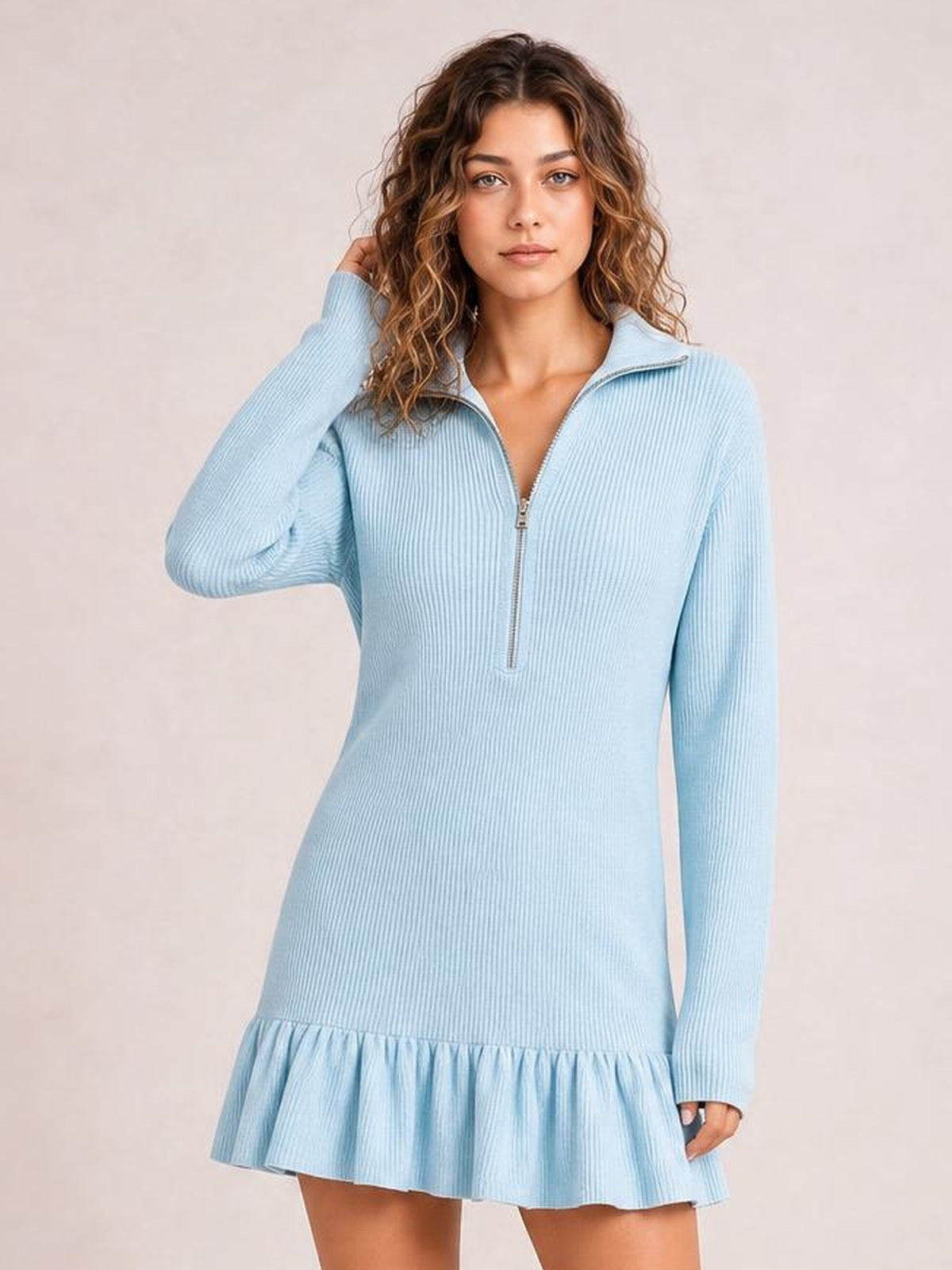 Model poses in a light blue ribbed dress with long sleeves, a half-zip neckline, fitted silhouette, and gathered ruffle hem.