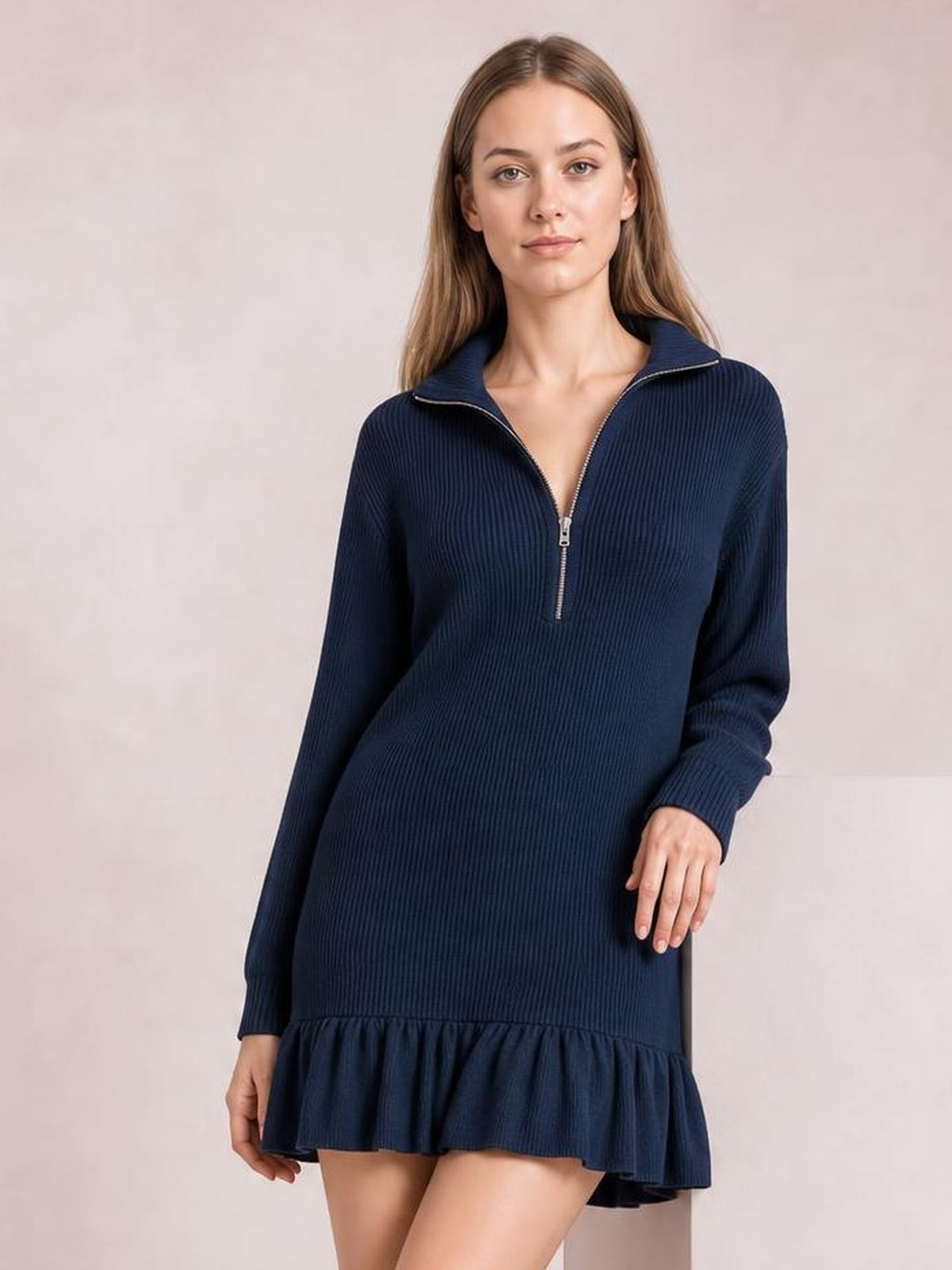 Model poses in a navy ribbed dress with long sleeves, a half-zip funnel neckline, relaxed silhouette, and flared ruffle hem.