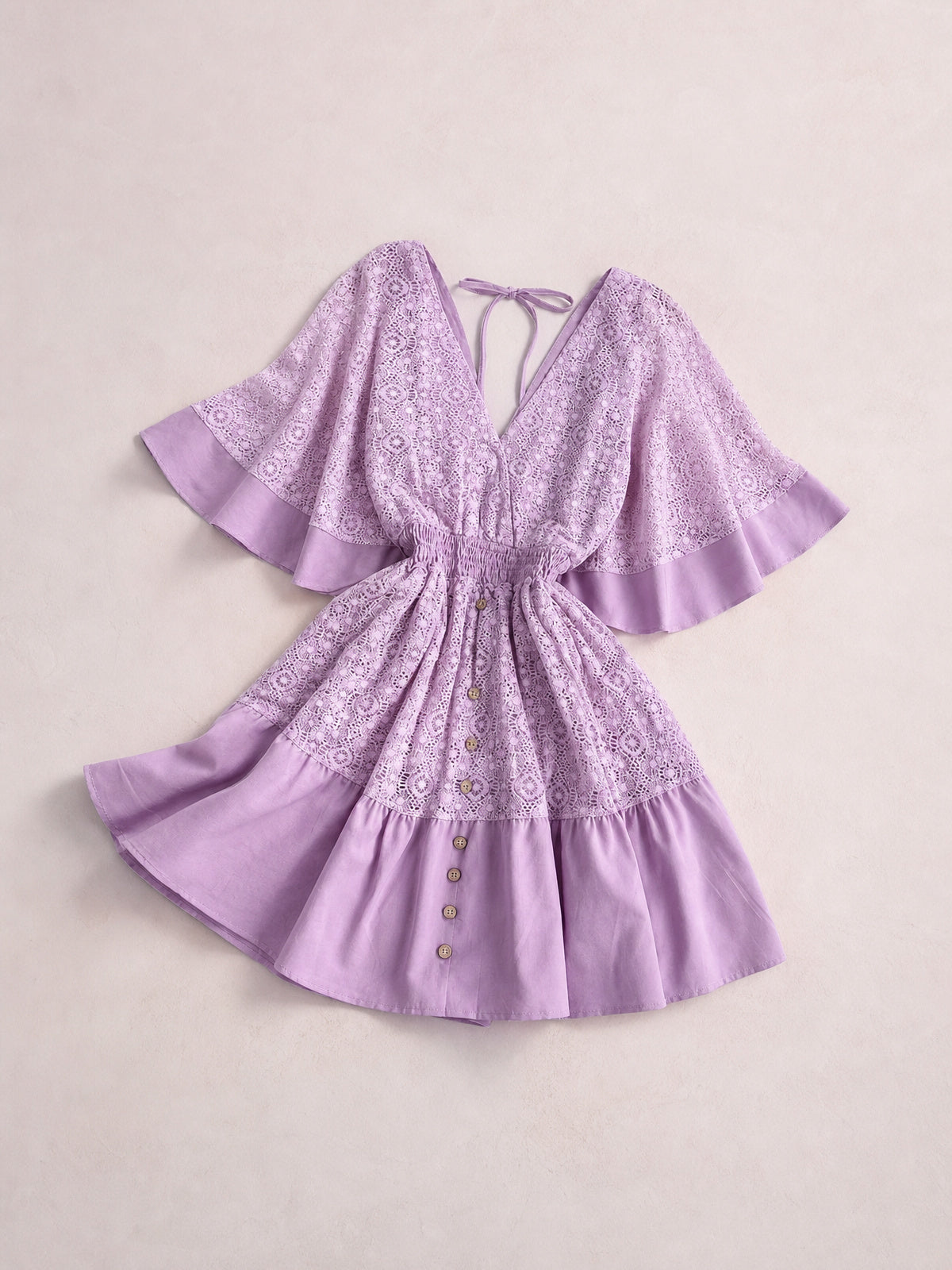 Lavender lace mini dress with a V-neck, tie-back opening, smocked waist, flared silhouette, bell sleeves, ruffled hems, and button-front skirt.