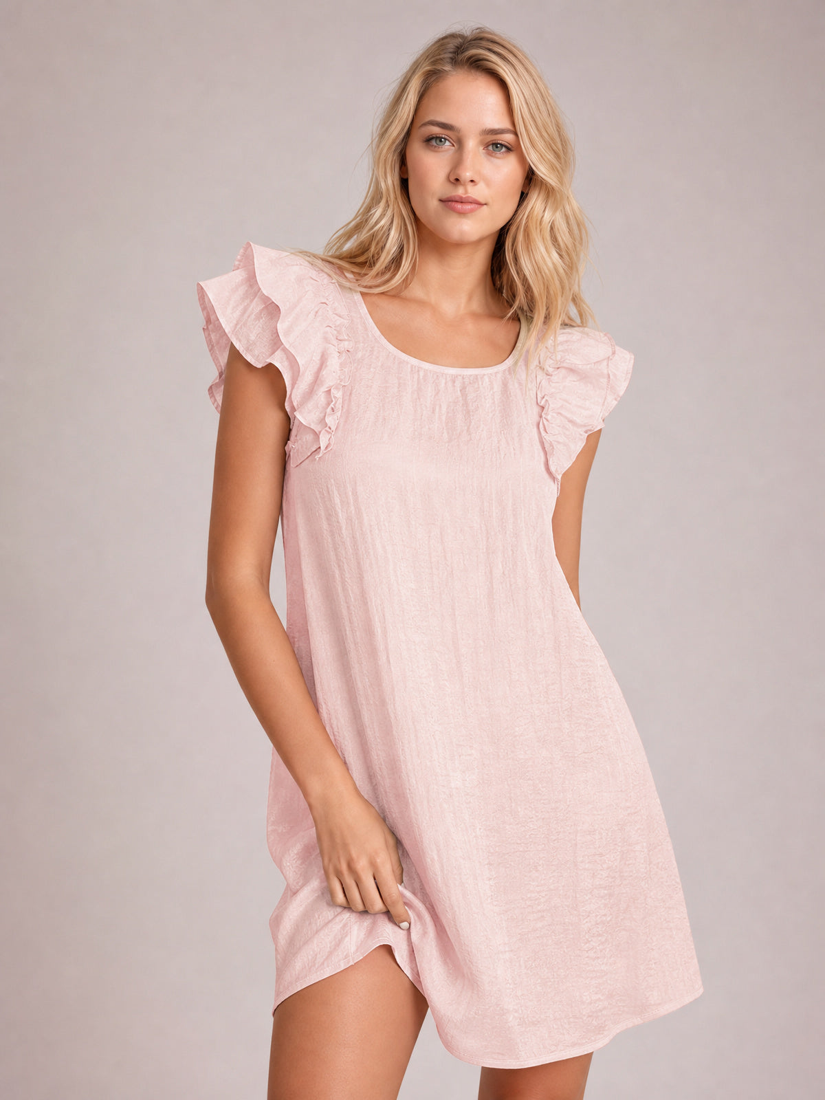Model poses in a watermelon pink mini dress with a relaxed silhouette, rounded neckline, fluttery ruffle sleeves, and a softly curved hem.