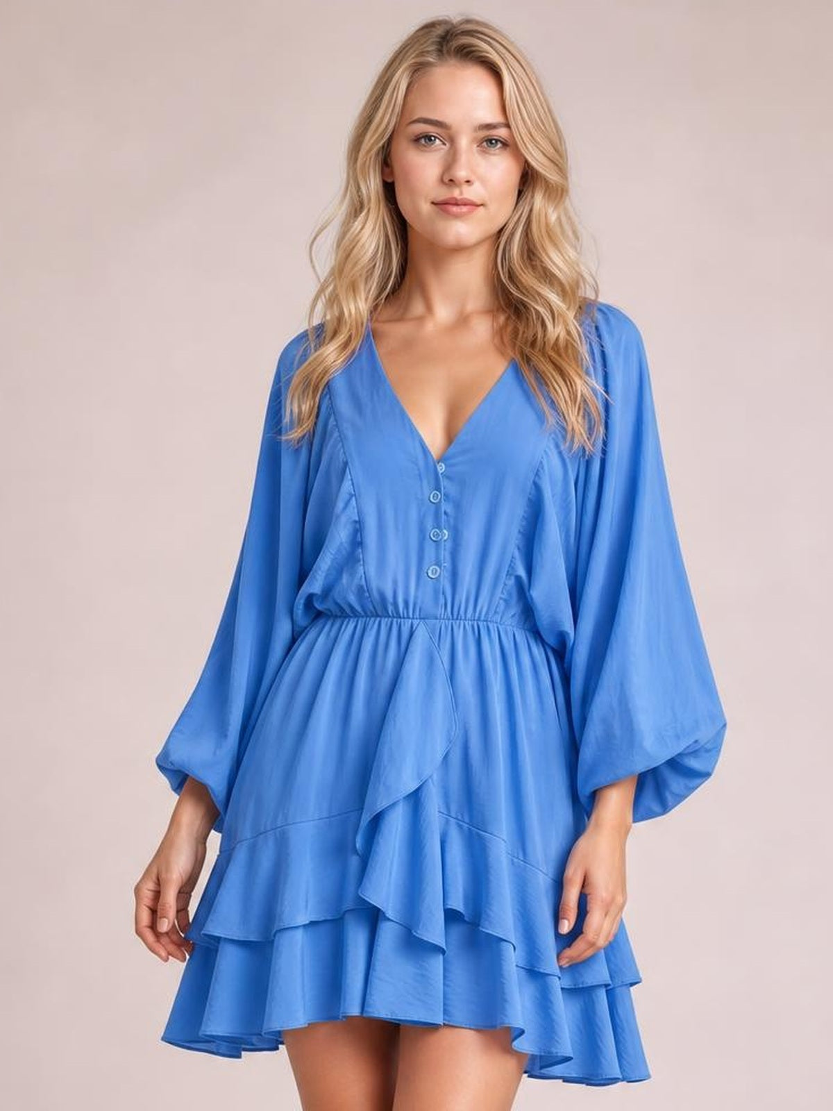 Model stands facing forward in a bright blue ruffled mini dress with a V-neck, decorative buttons, balloon sleeves, elastic waist, and tiered flounced skirt.