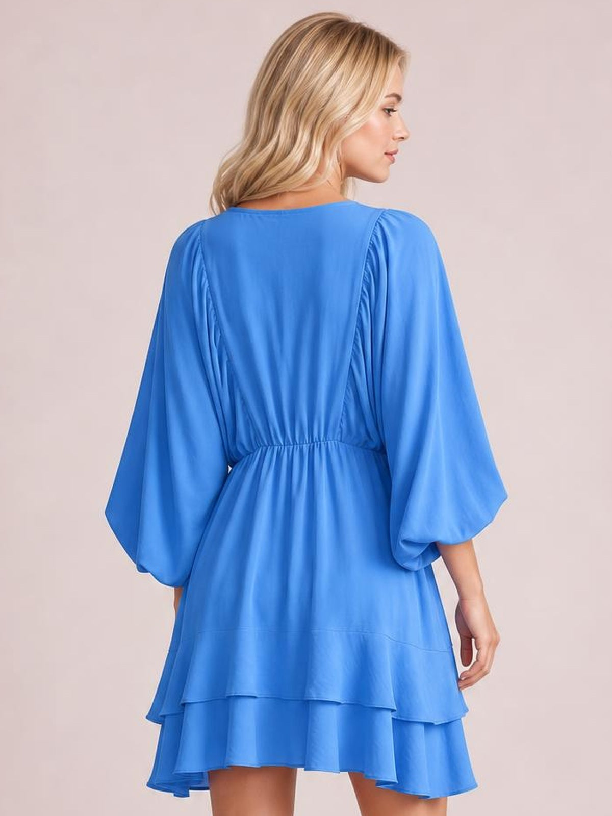 A model shown from behind wears a bright blue ruffled balloon sleeve mini dress with an elastic waist and layered tiered skirt.