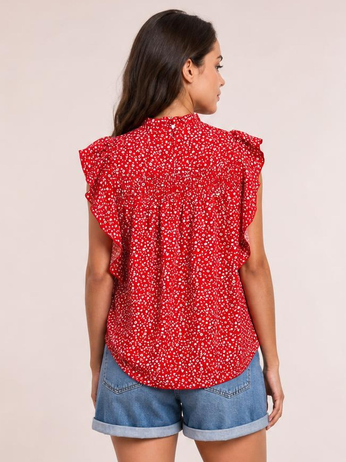 A model shown from behind wears a red ditsy floral blouse with a smocked back, mock neck, ruffled cap sleeves, and a relaxed curved-hem silhouette.