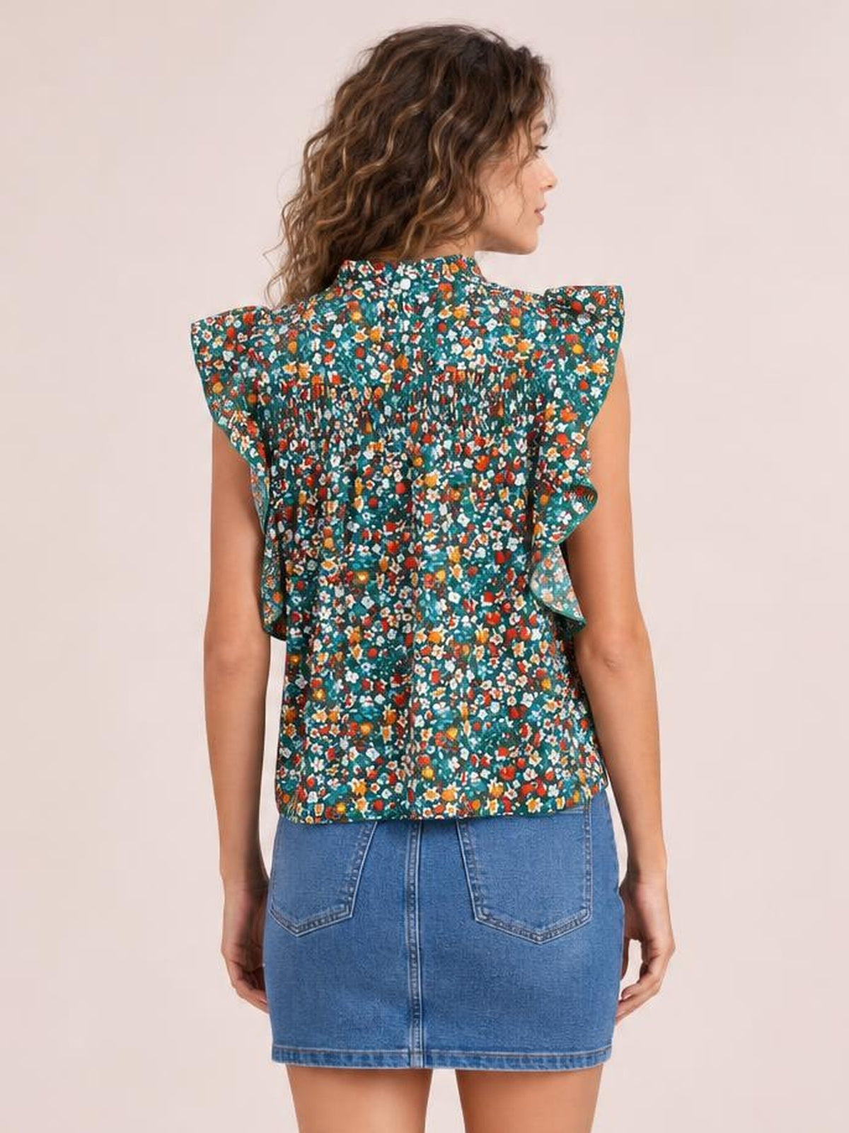 Model shown from behind in a teal ditsy floral blouse with a ruffled mock neck, cap sleeves, smocked back, and relaxed straight silhouette.