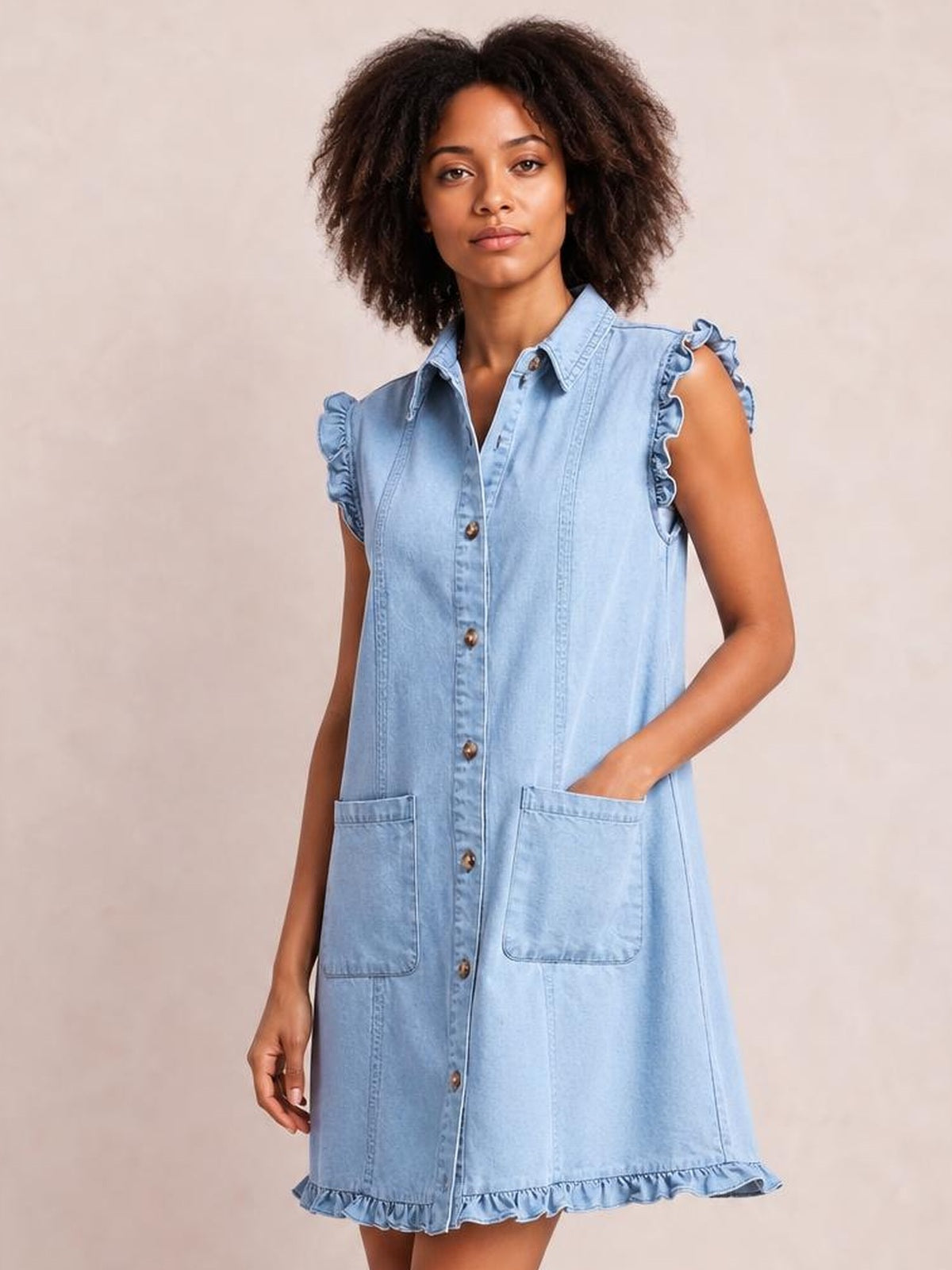 Model wearing a light blue denim shift dress with a collared button front, ruffled cap sleeves and hem, vertical seams, and two front pockets.